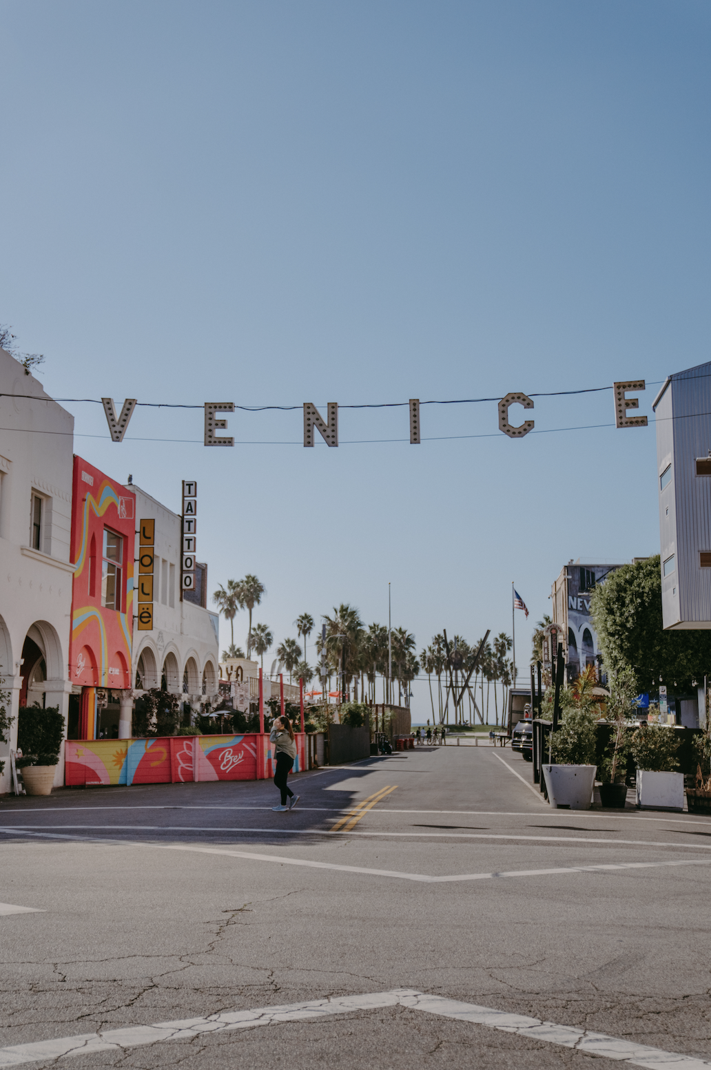 Street view of Venice, California with large decorative letters spelling out 'VENICE' across the street, palm trees, and colorful storefronts.
