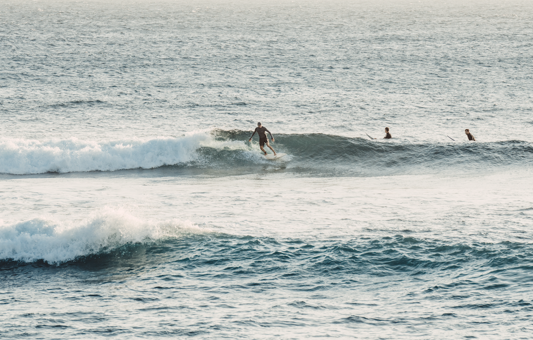 Surfer riding a wave while three paddleboarders follow behind in the ocean.