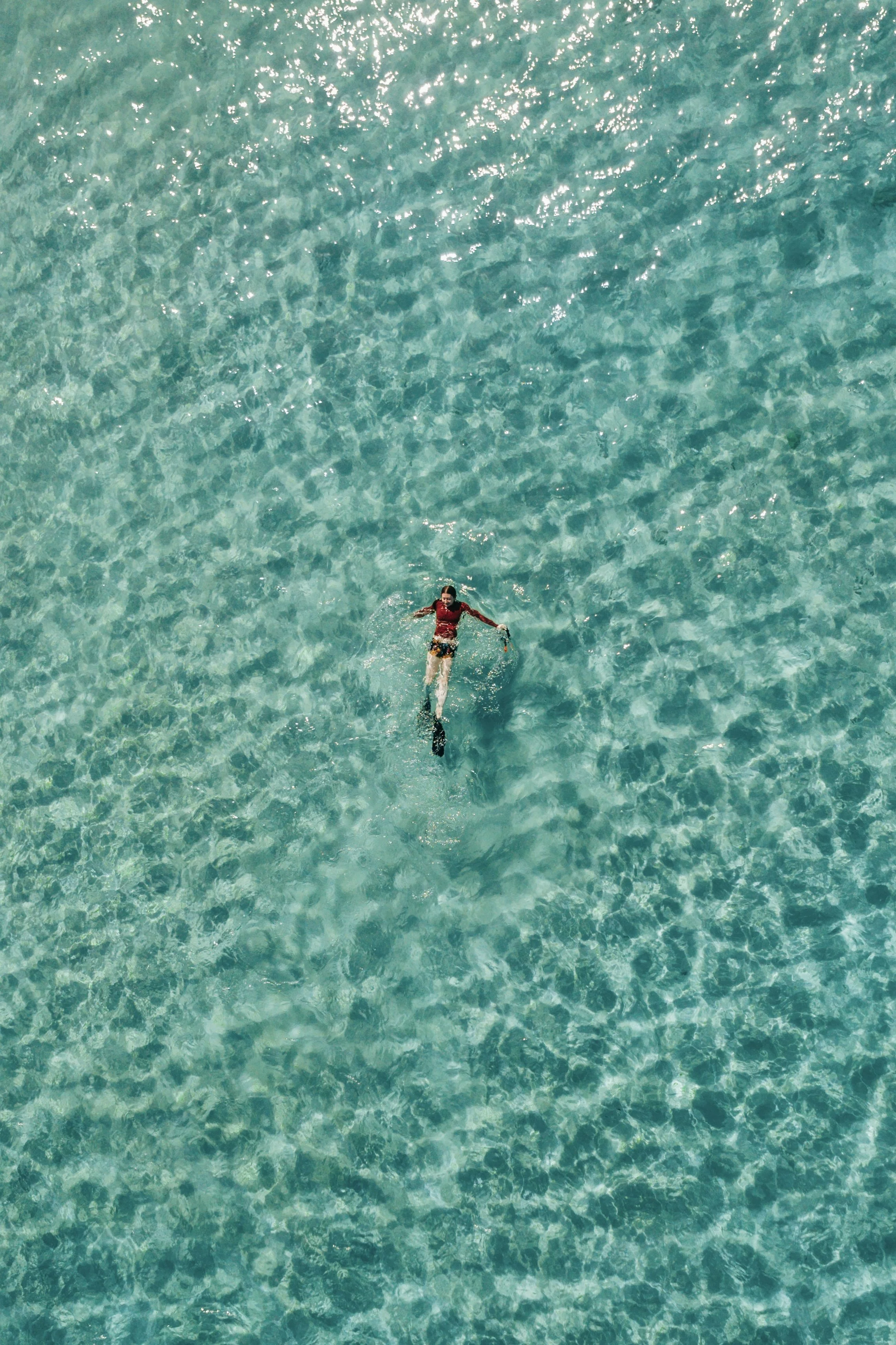 Aerial view of a person swimming in clear turquoise water.