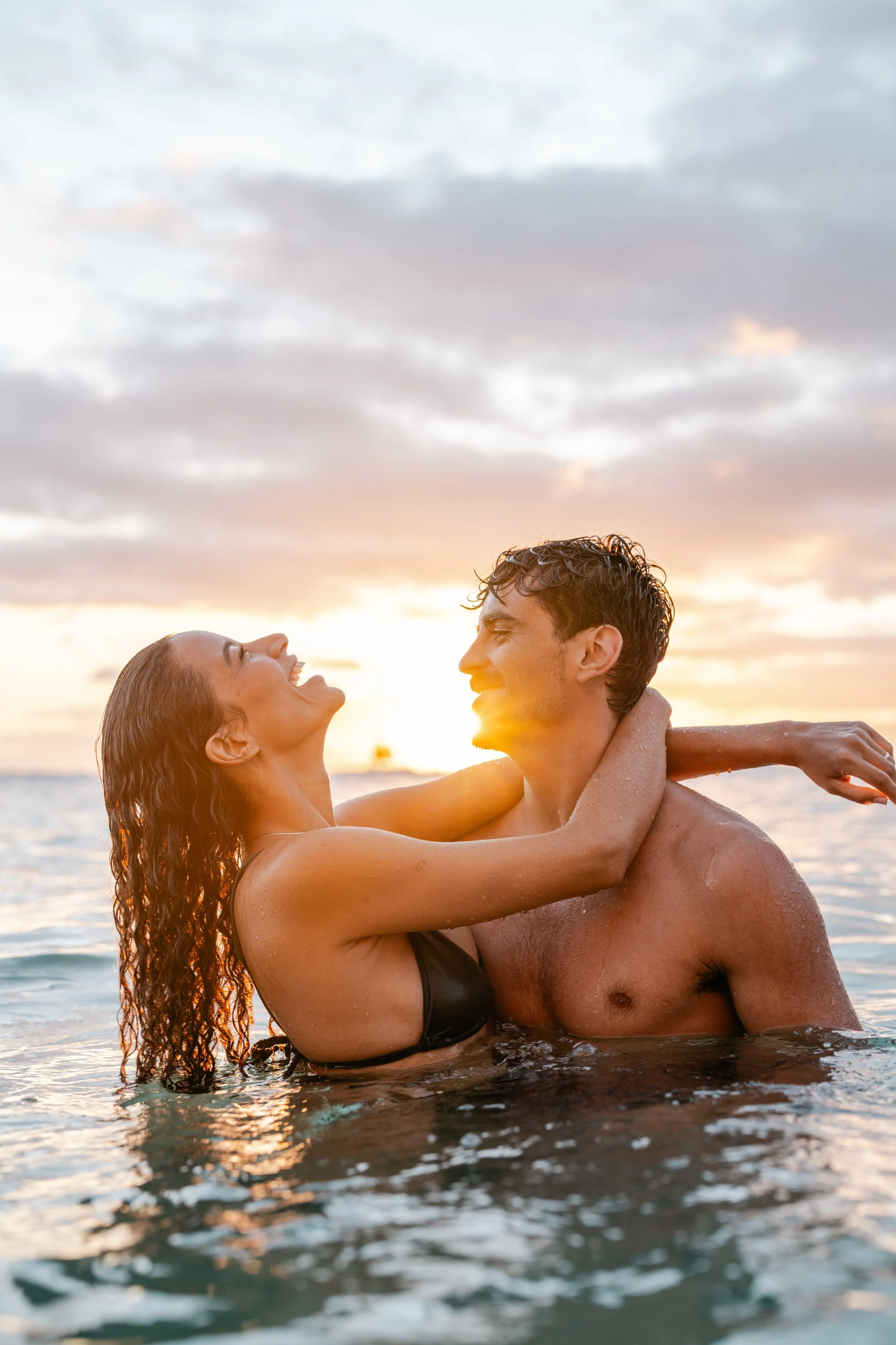 A smiling couple enjoying their time in the water at sunset, with the sunset sky in the background.