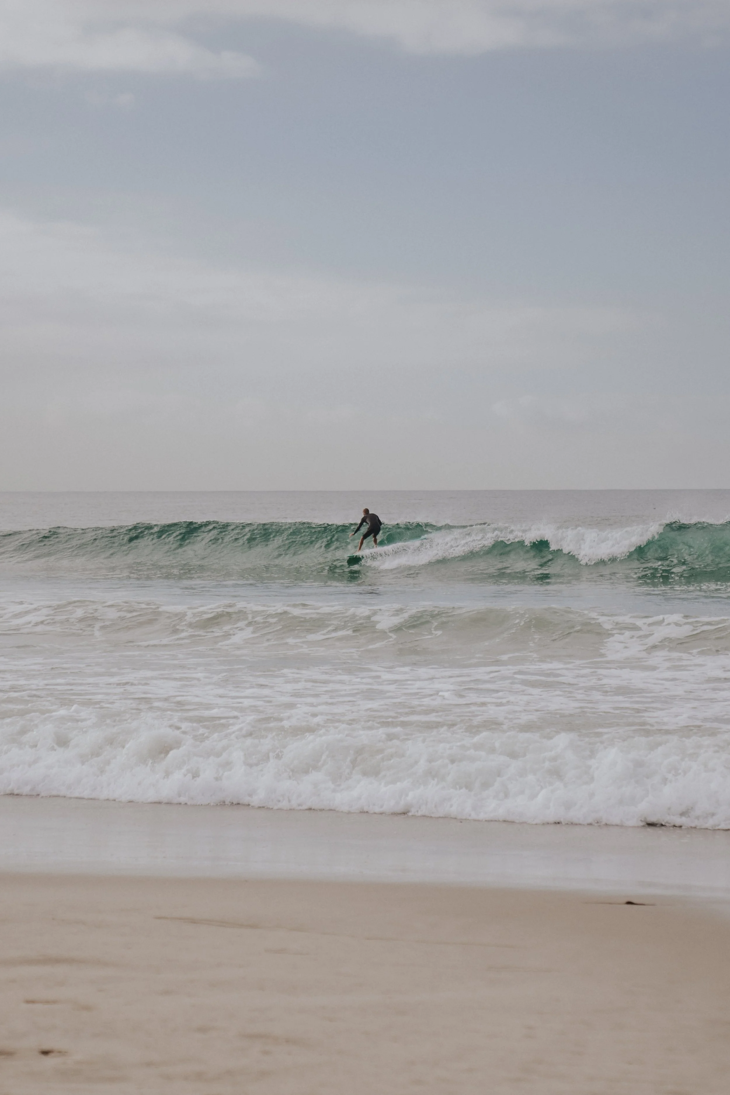 A person surfing on a wave at the beach with overcast skies.