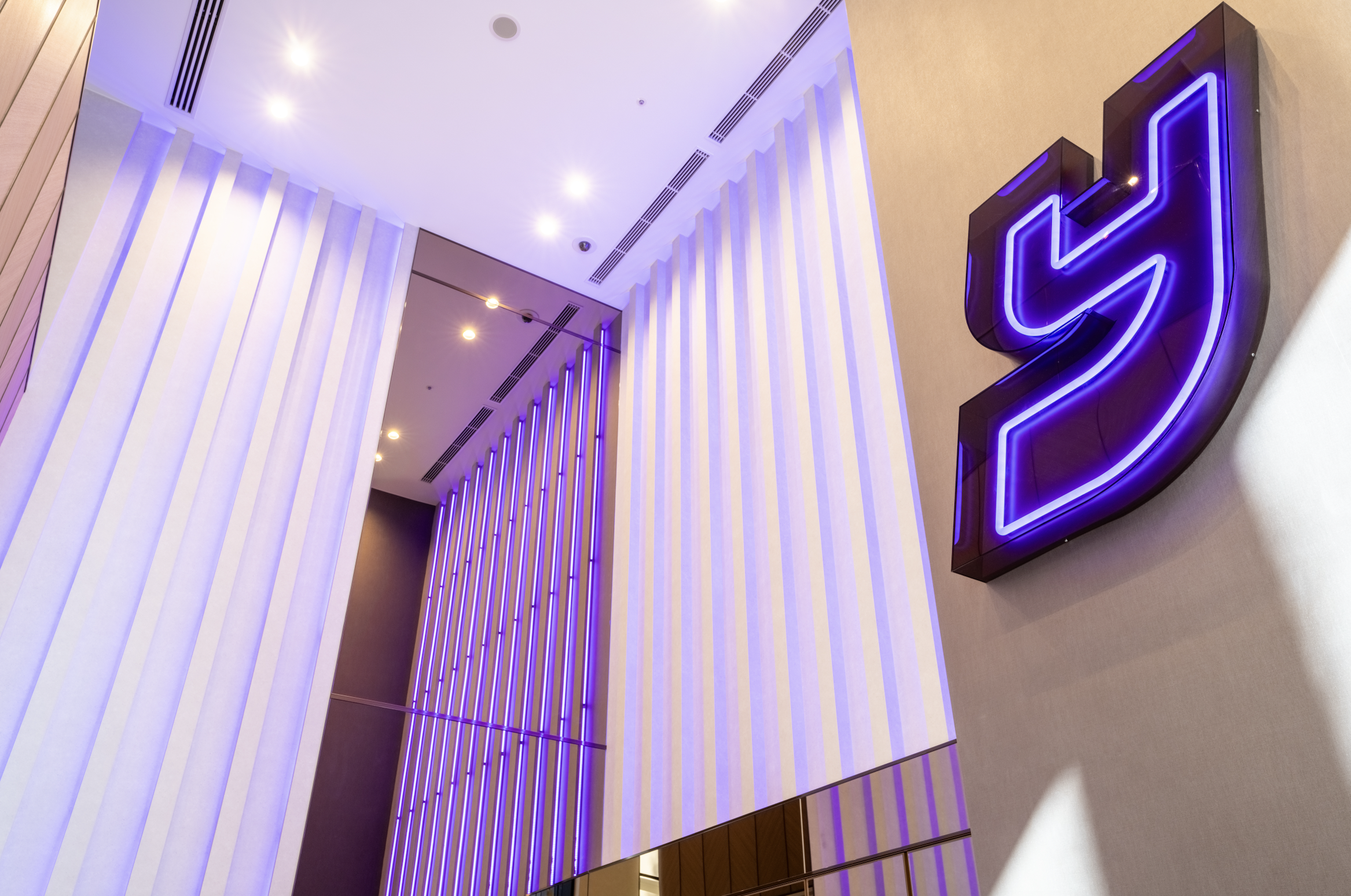 Modern interior with a large illuminated neon sign on the wall, vertical purple lighting accents, and a ceiling with built-in lighting