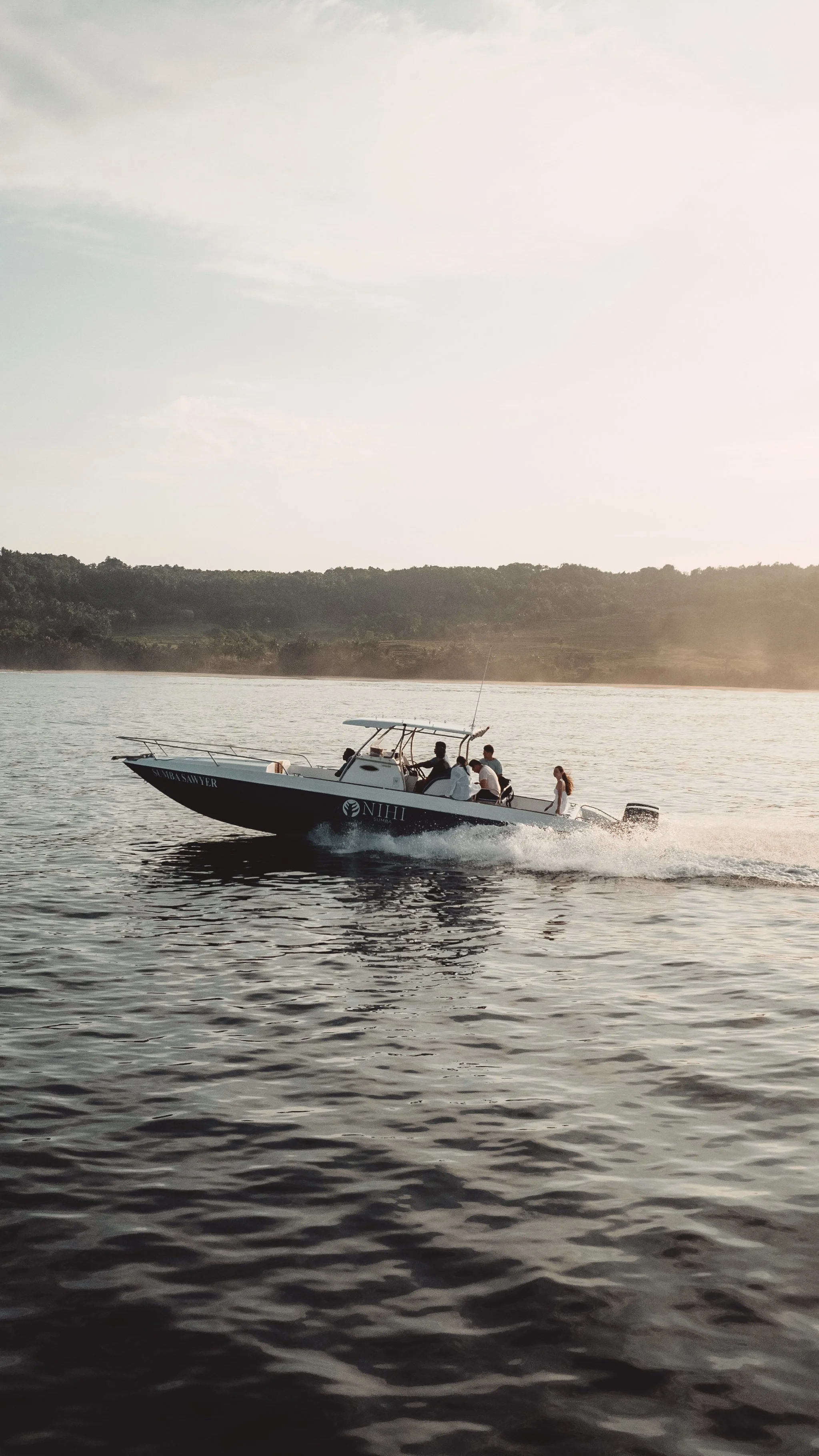 A boat with people on board moving across a lake at sunset.