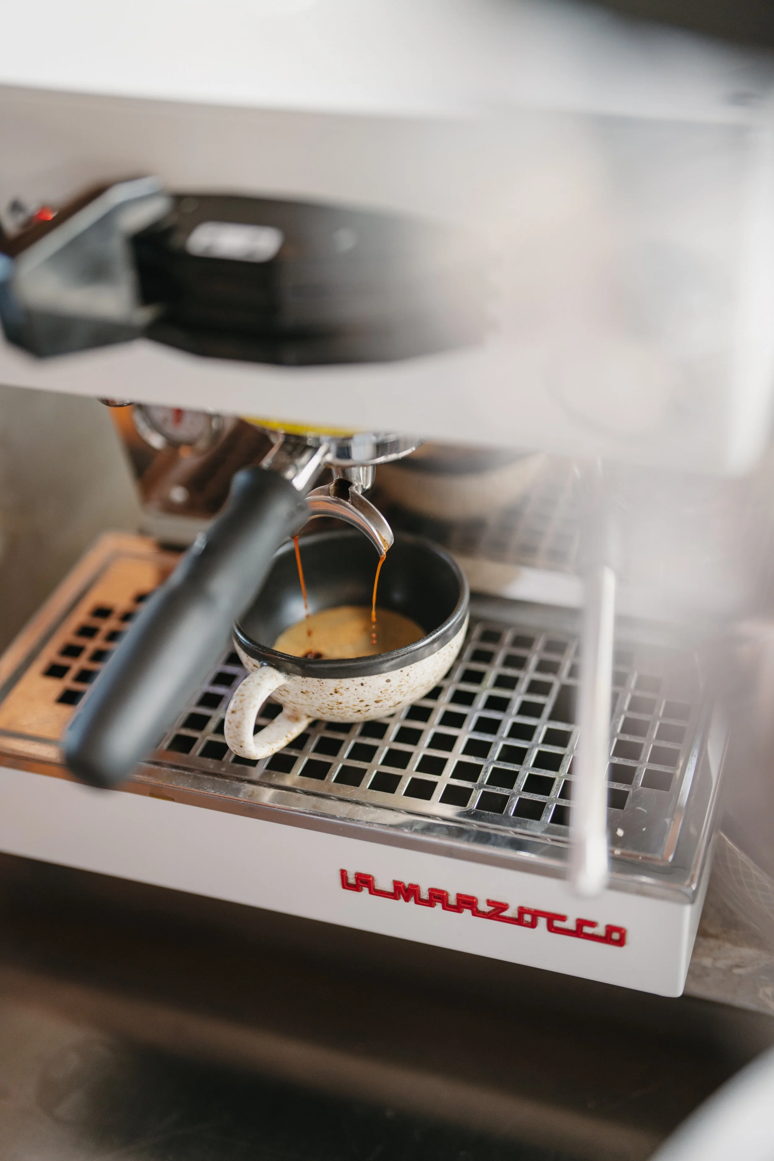 Espresso machine brewing coffee into a ceramic cup with hot coffee dripping from the spout.