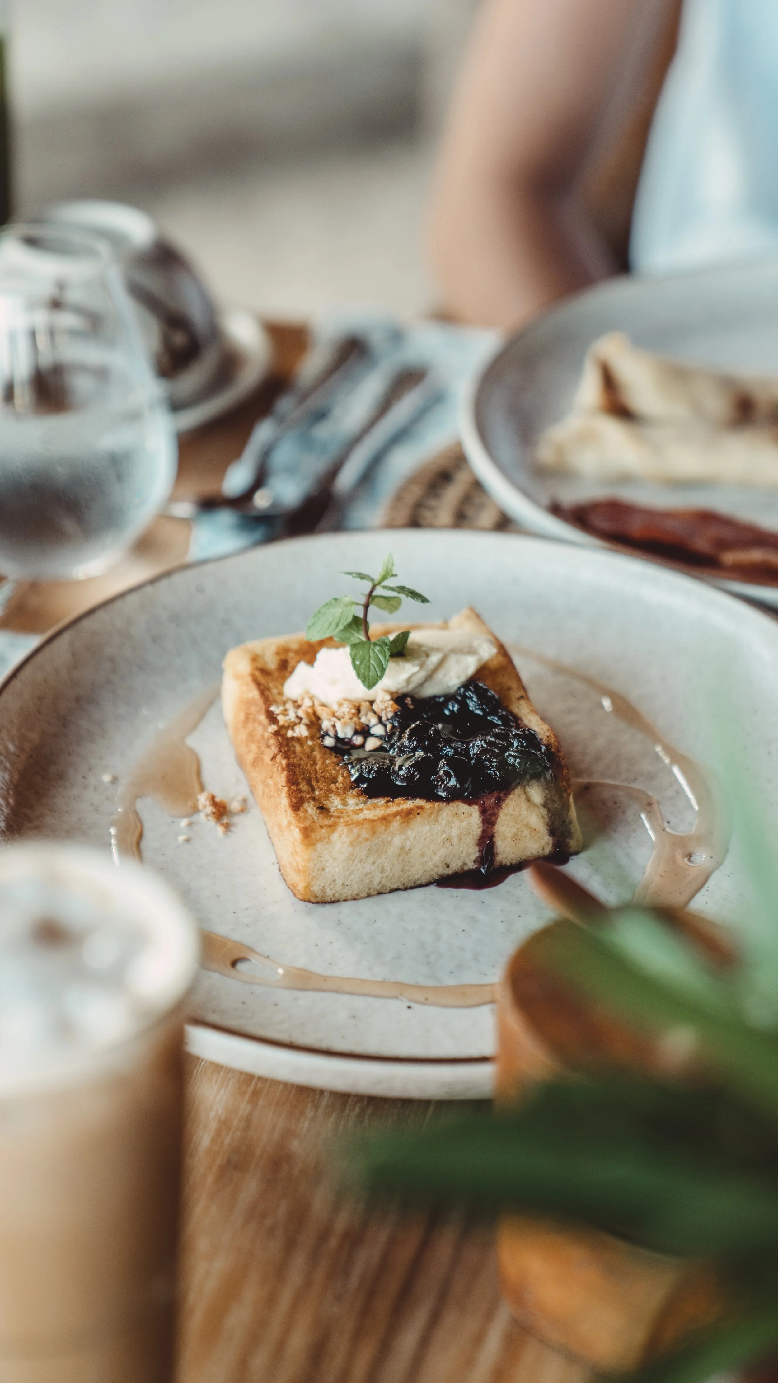 A slice of French toast topped with whipped cream, blueberries, and a mint leaf, garnished with honey on a round beige plate.