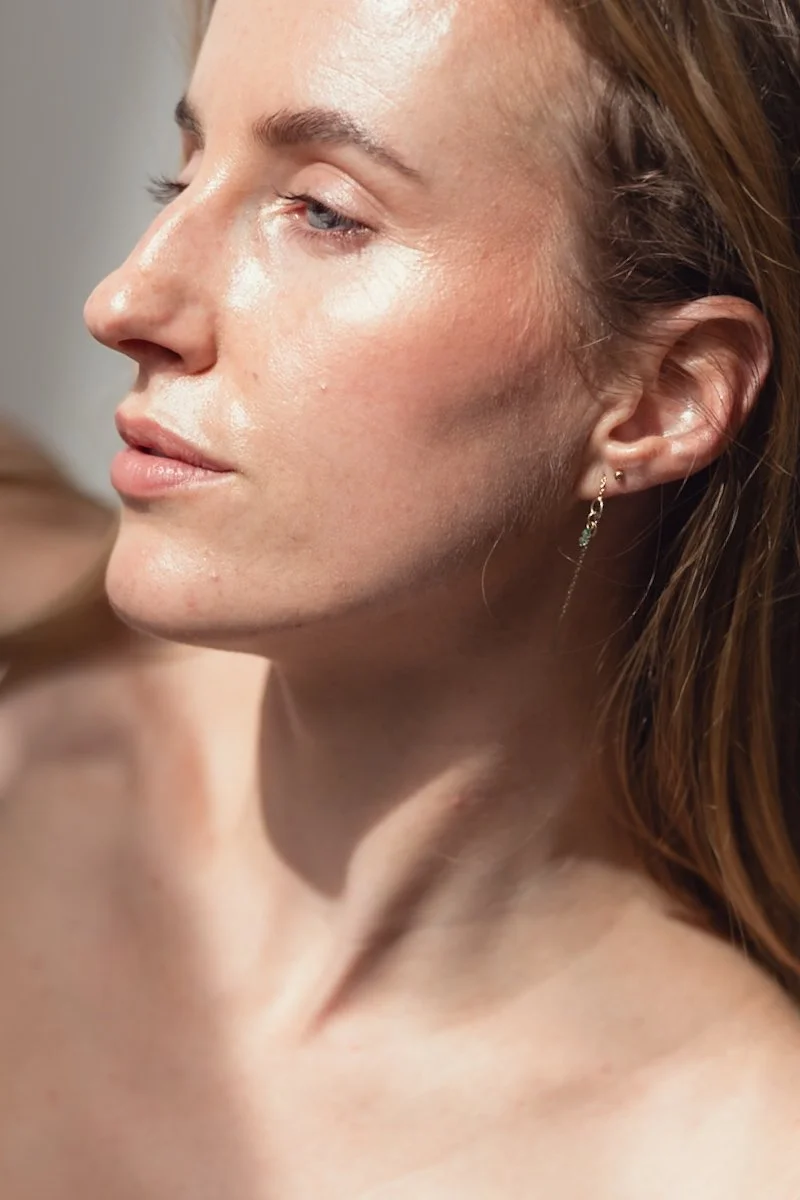 Close-up van een vrouw met licht getinte huid, korte bruin haar en een enkele oorbel, met een ontspannen en zelfverzekerde uitdrukking.