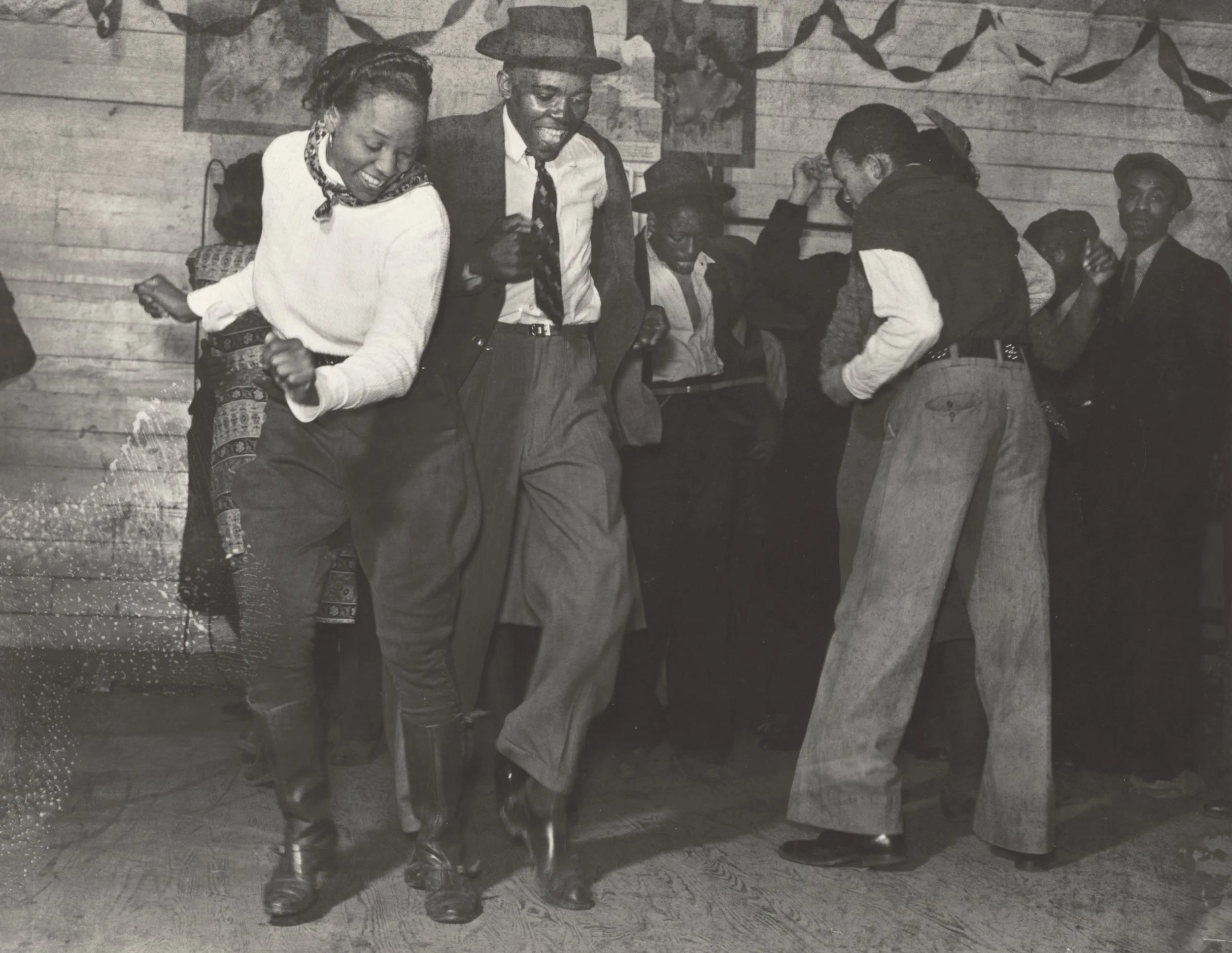 Group of people dancing and enjoying themselves at a social gathering, with some seated in the background.