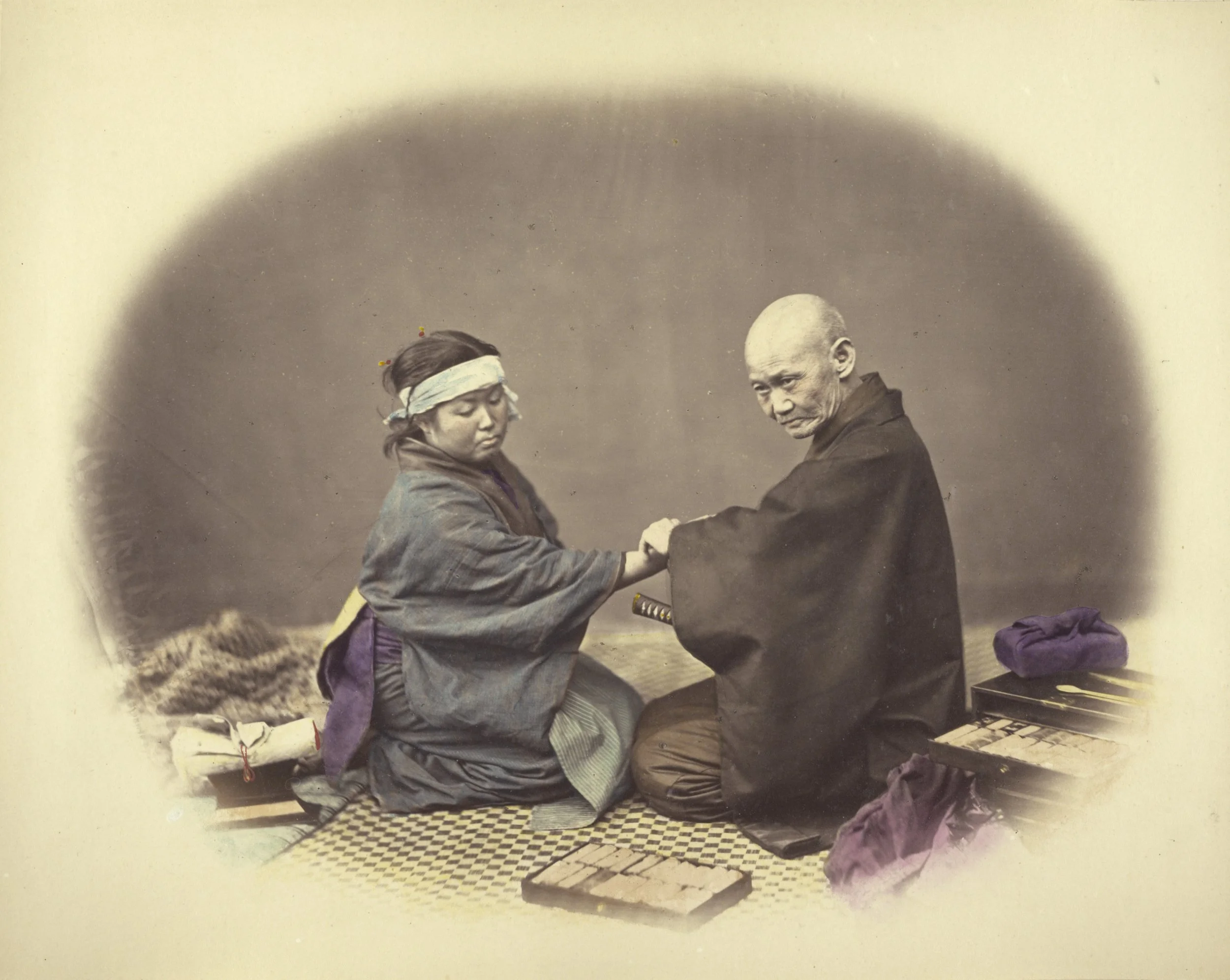 A sepia-toned photograph depicts a young girl in traditional Japanese clothing fitting or presenting a small sword to a seated elderly man who appears to be a monk or samurai.