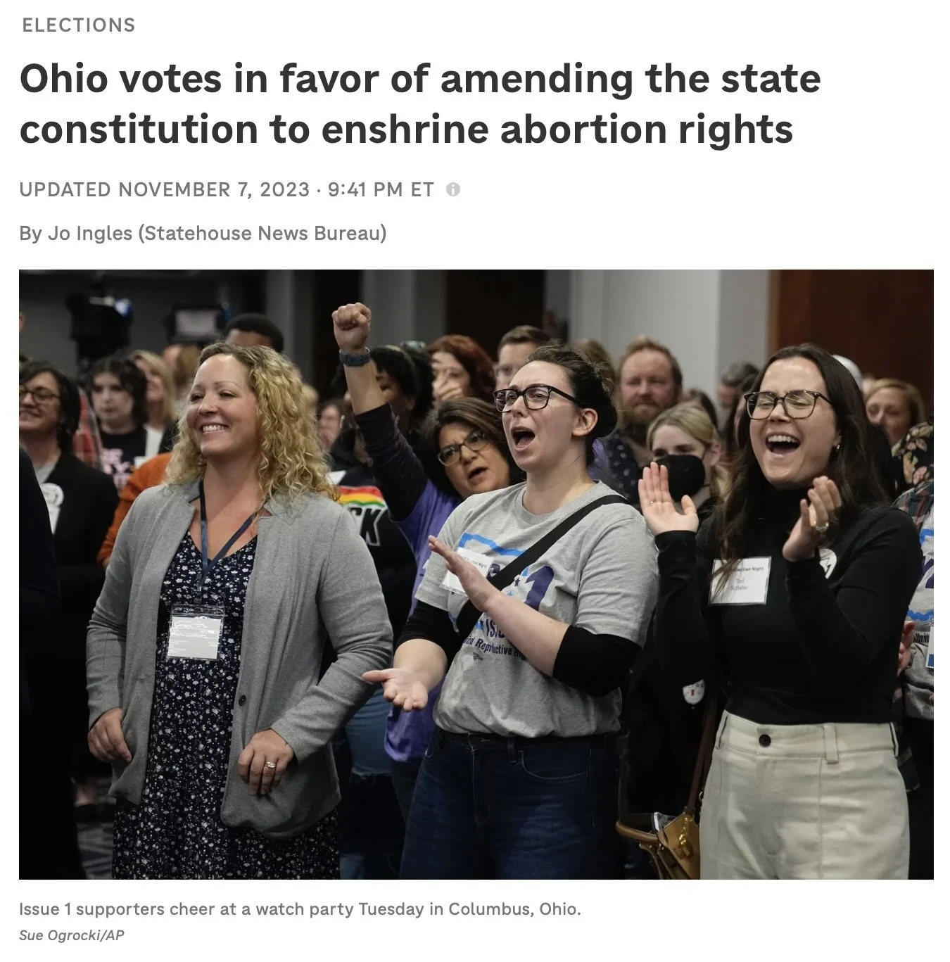A group of people cheering and celebrating at a watch party in Columbus, Ohio, with some raising fists and others clapping, showing excitement over election results.
