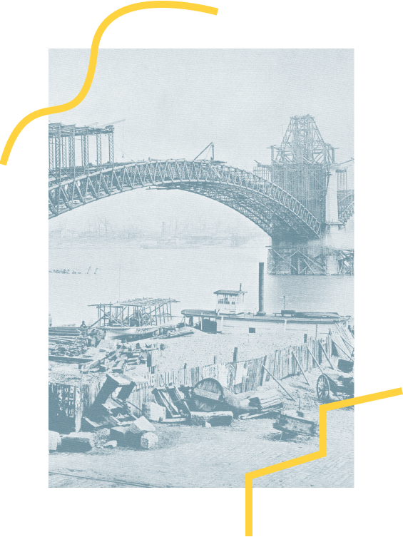 Black and white photograph of a bridge under construction over a river, with construction equipment and debris on the riverbank.