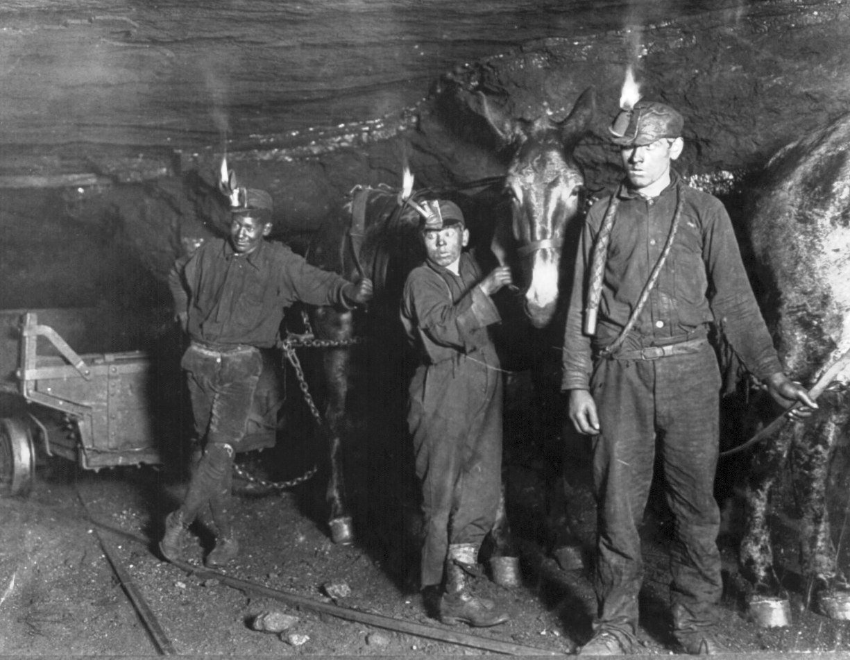Three miners with headlamps in a cave, one with a horse, all wearing work clothes.