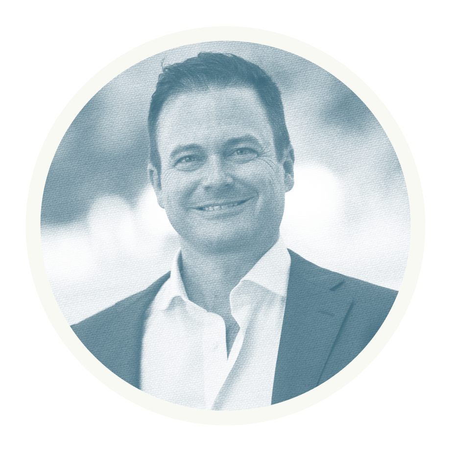 A professional headshot of a man in a suit smiling, with a cloudy sky in the background.