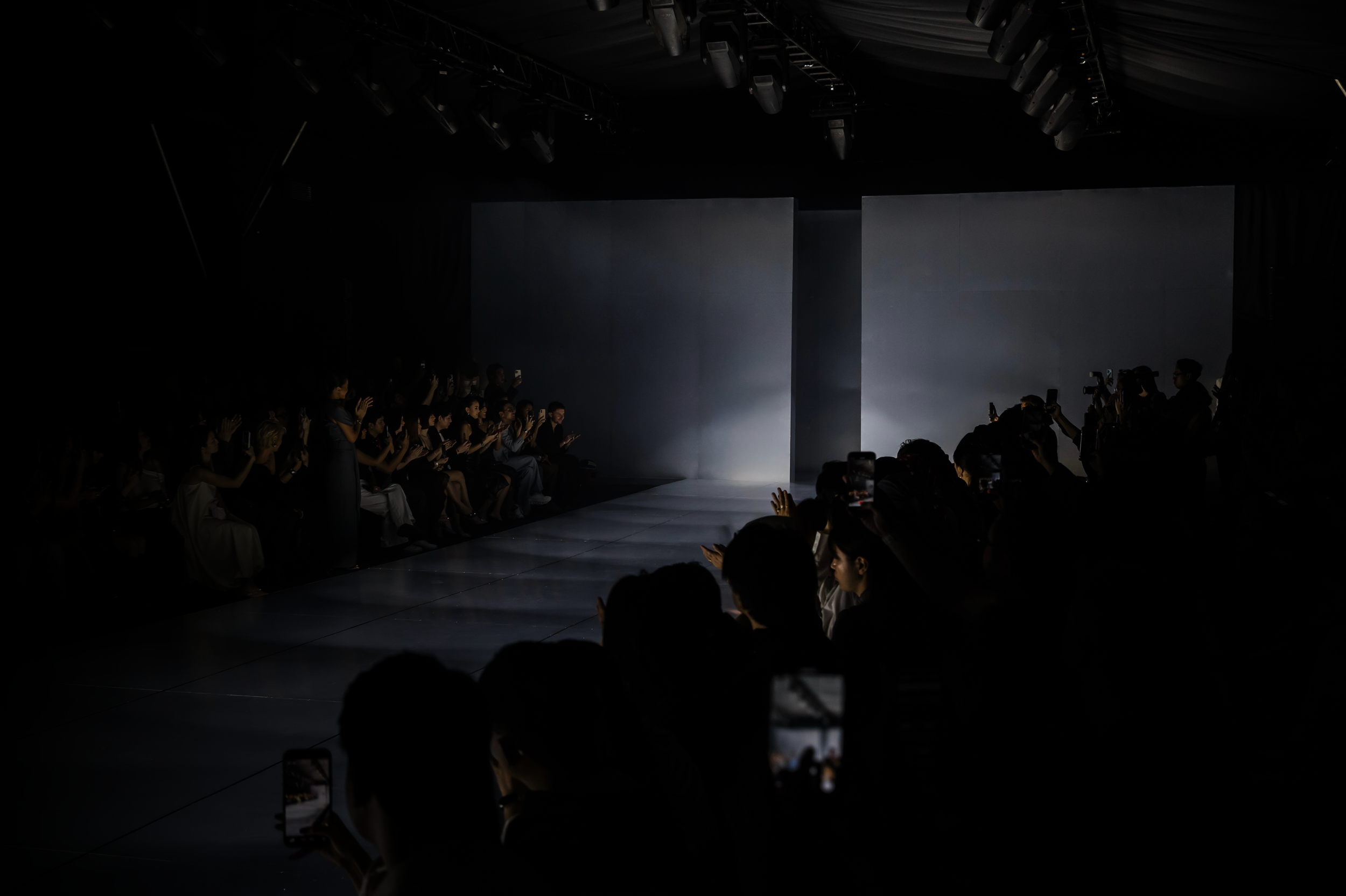 Fashion runway production with structured staging and audience in low light.