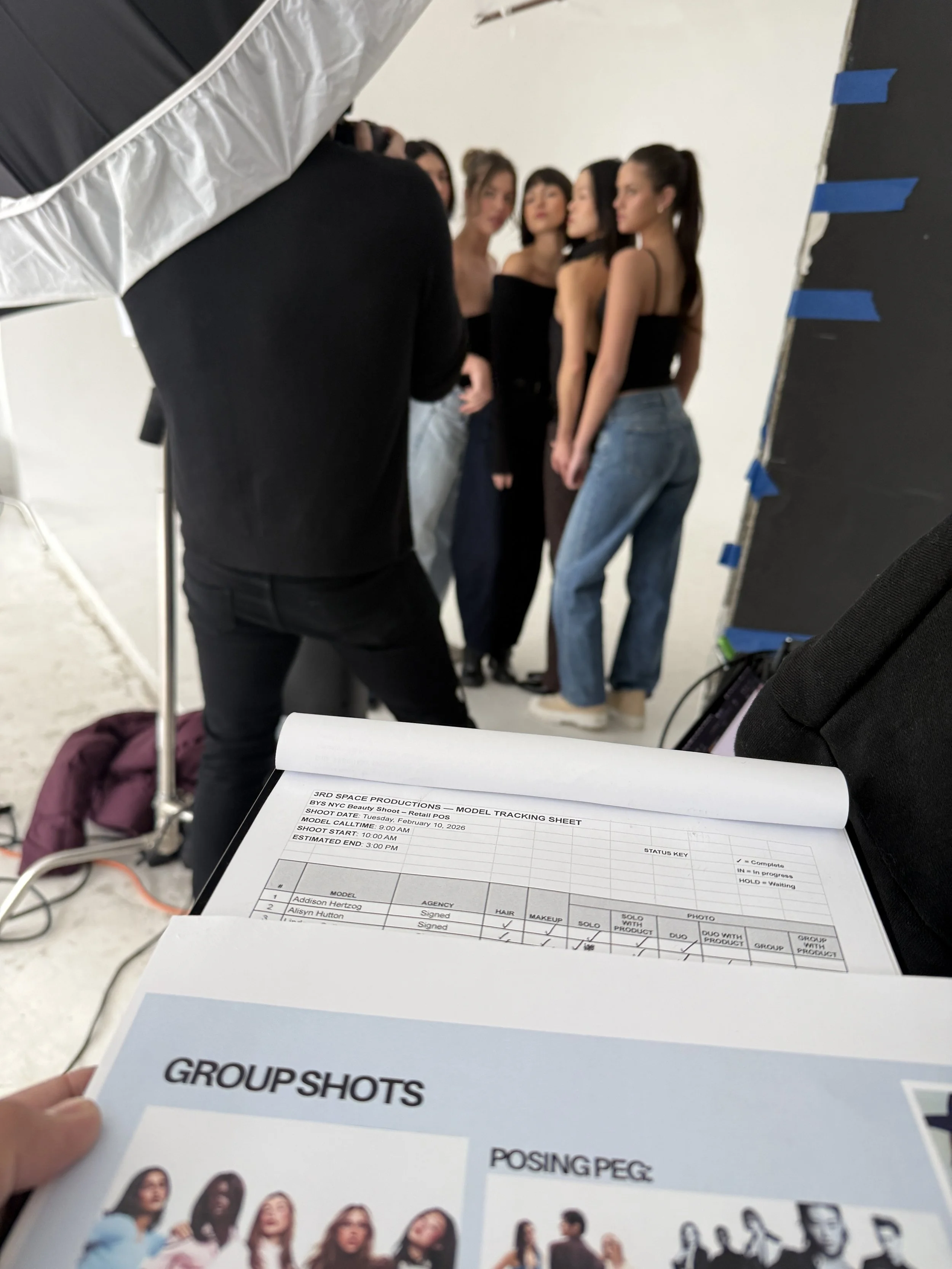 Photographer capturing a group of models, with a 3rd Space Productions model tracking sheet in the foreground during the BYS Cosmetics shoot.