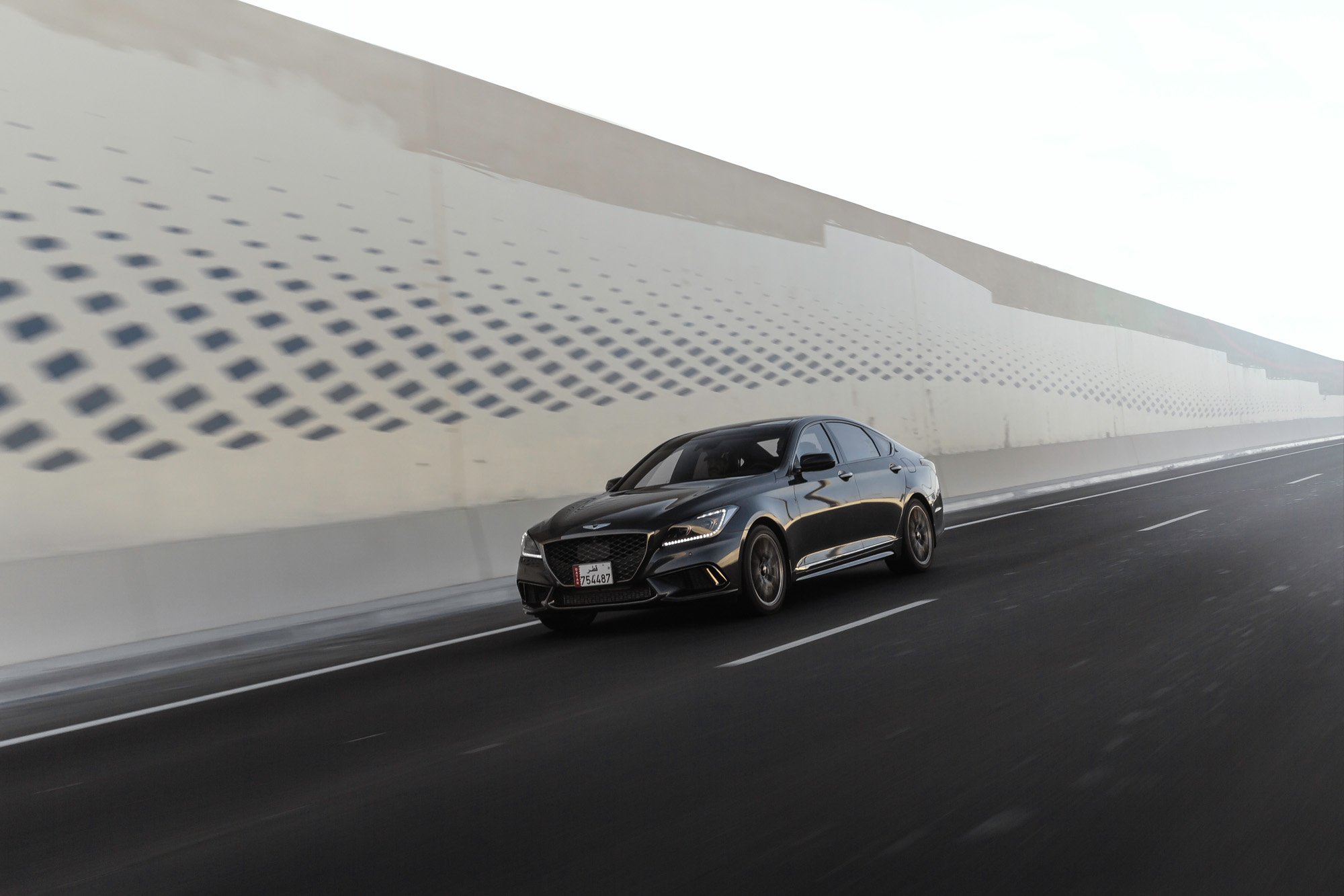 Genesis G70 driving on an empty highway in West Bay Dafna with a modern white tunnel wall on the side in Doha, Qatar.