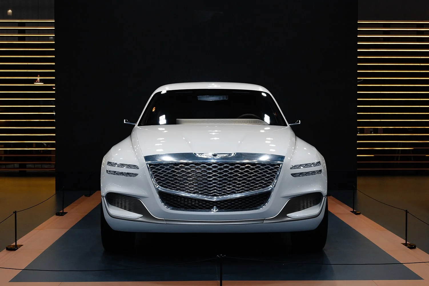 Front view of a white luxury sedan on display in a showroom with black and gold decor.