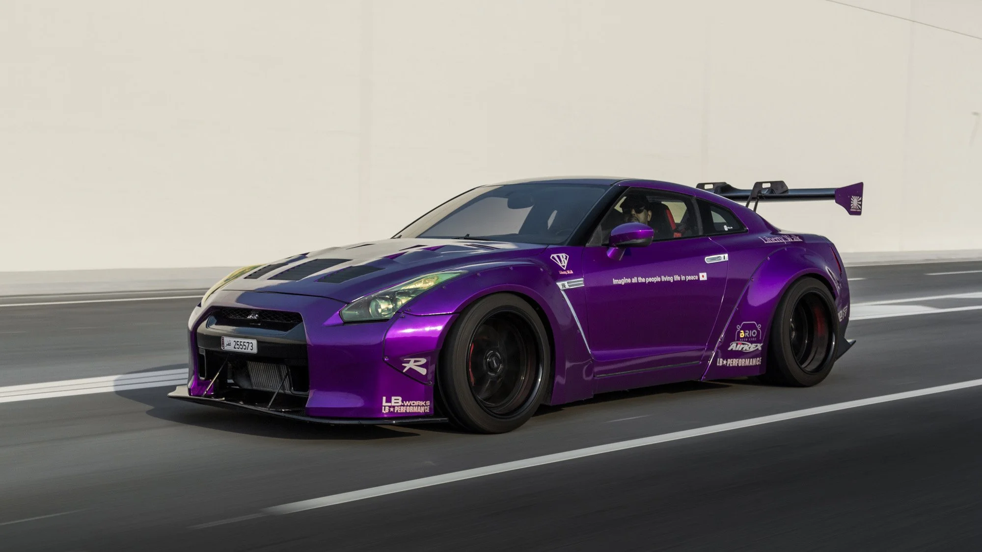 Purple race car on a track with a black rear wing and various sponsor stickers.