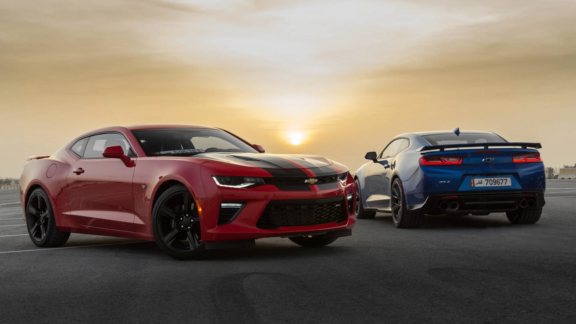 Two Chevrolet Camaro from Al Jaidah Motors, parked on an empty lot with a sunset sky in the background at Doha, Qatar.