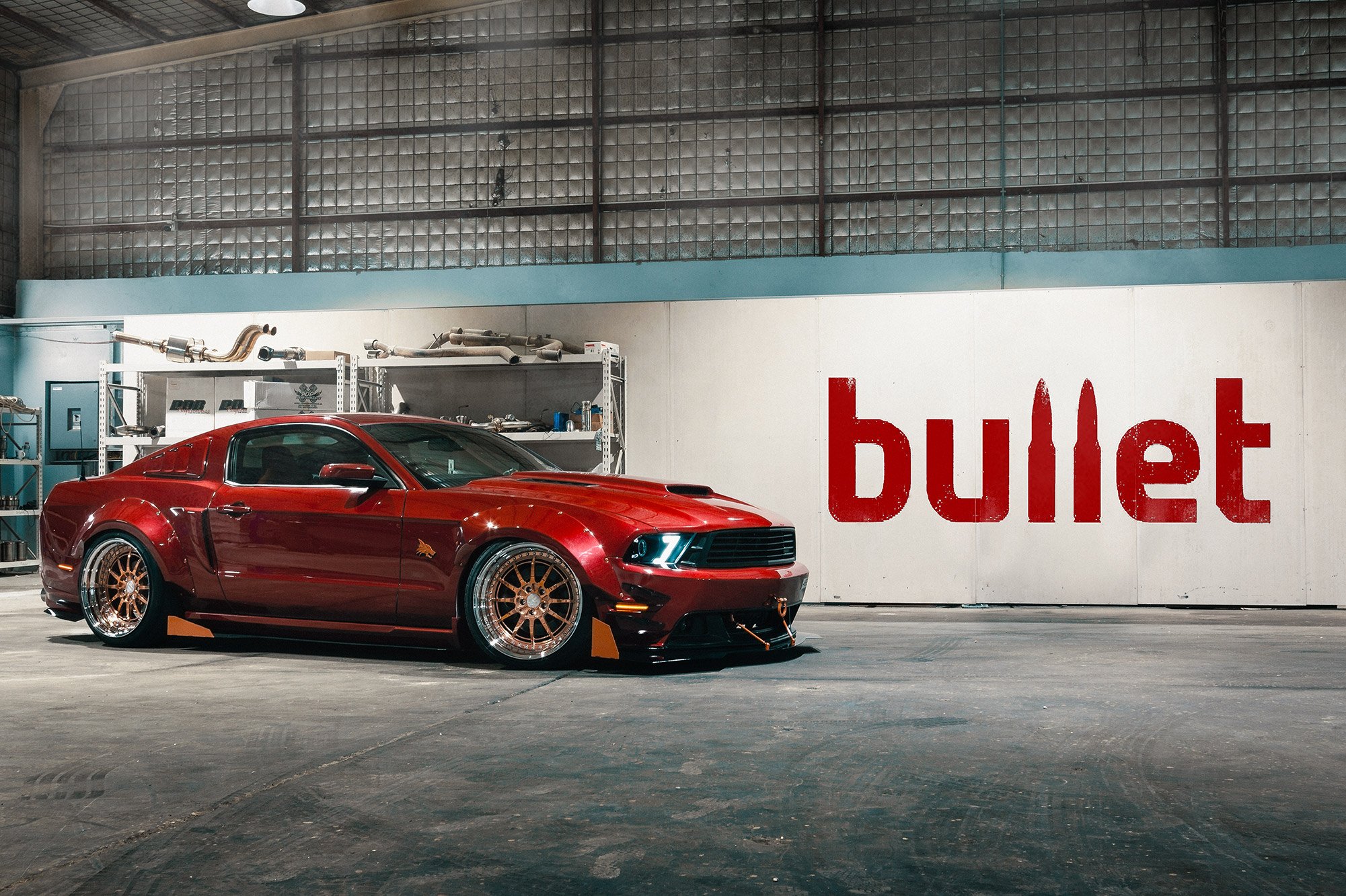A Ford Mustang GT with gold rims parked in an indoor garage with a large 'bullet' sign on the wall. Bullet Garage in Doha, Qatar.