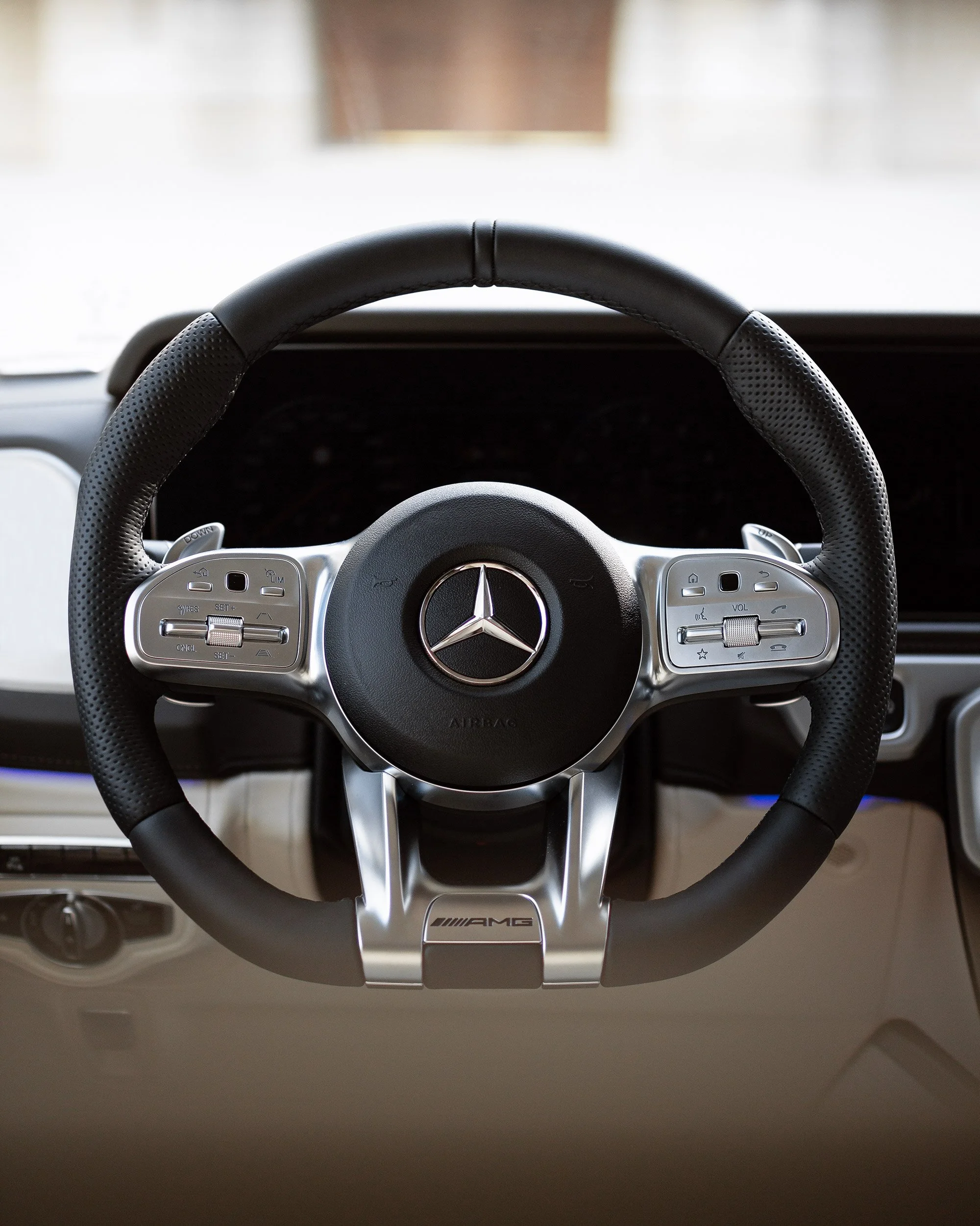 Close-up of a Mercedes-Benz AMG car steering wheel with control buttons, steering column, and part of the dashboard visible.