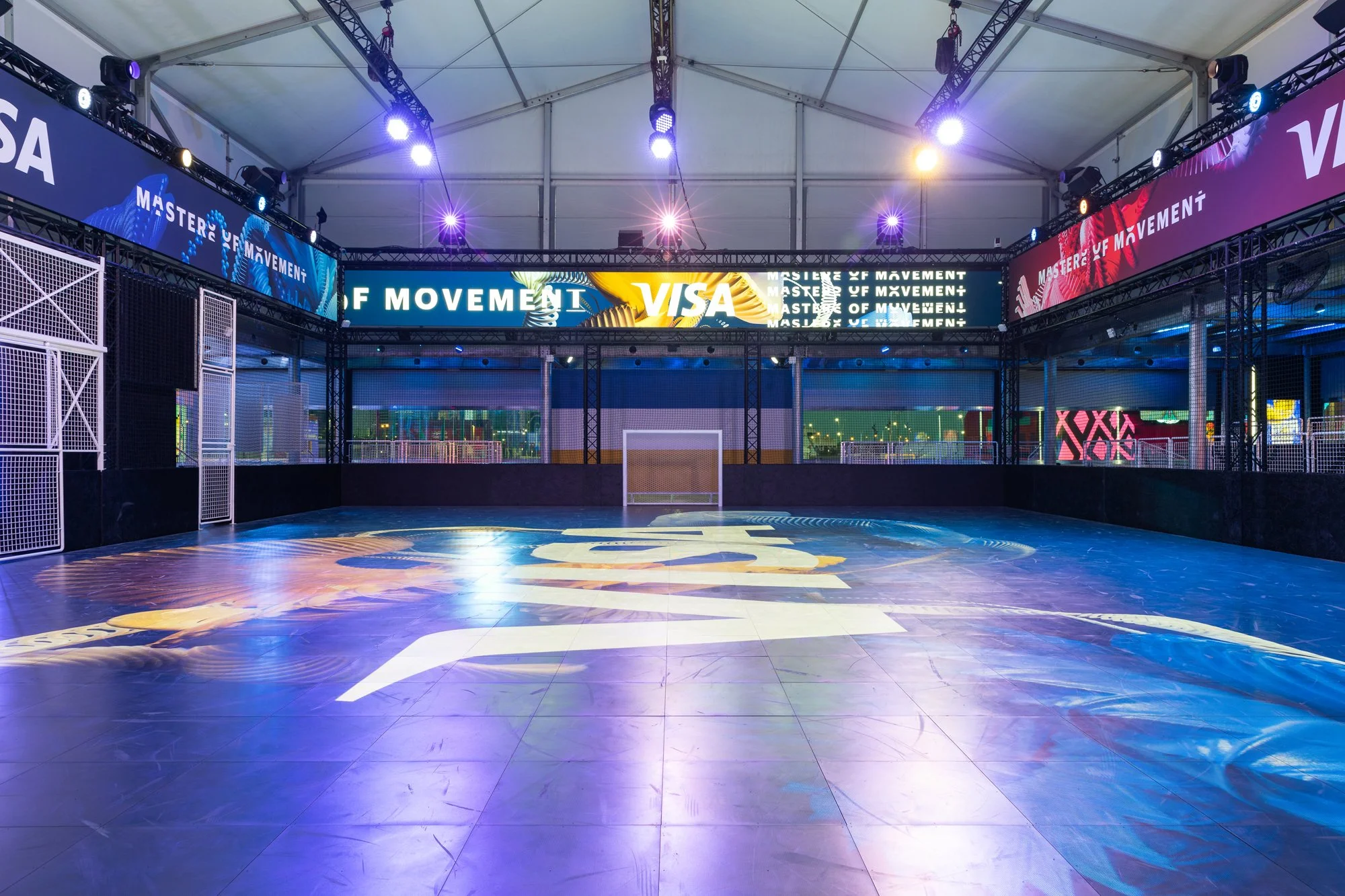 Empty indoor sports arena with illuminated digital banners and a soccer goal at the back.
