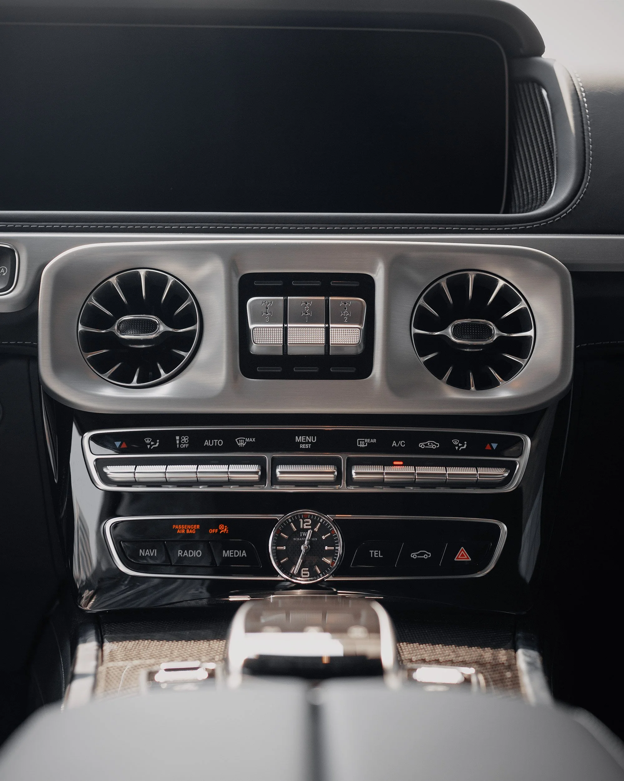 Dashboard of a luxury car with air vents, control buttons, and a clock.