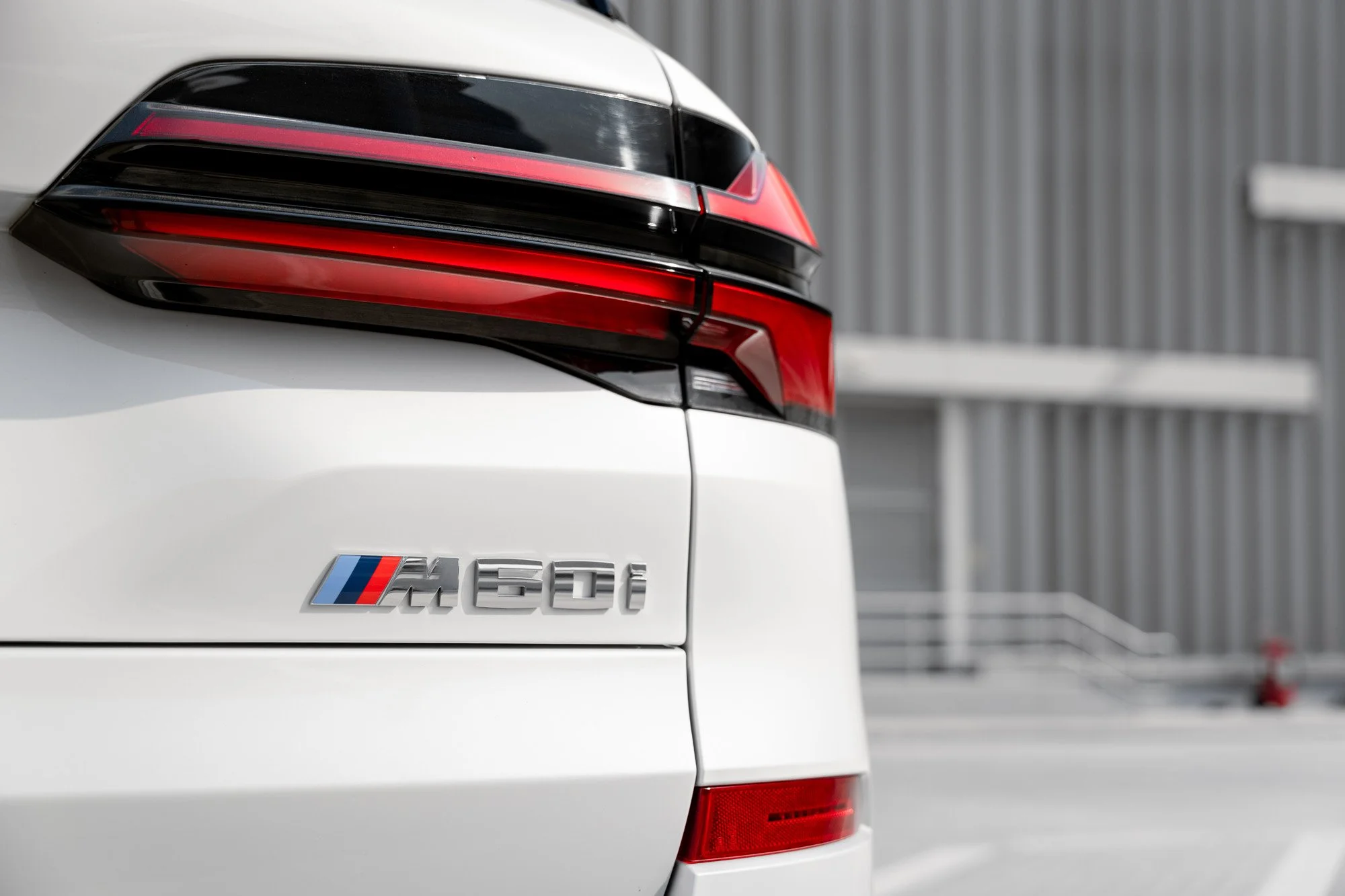 Close-up of a white BMW X5 M60i vehicle focusing on the rear with M logo badge, taillight, and parking area background.