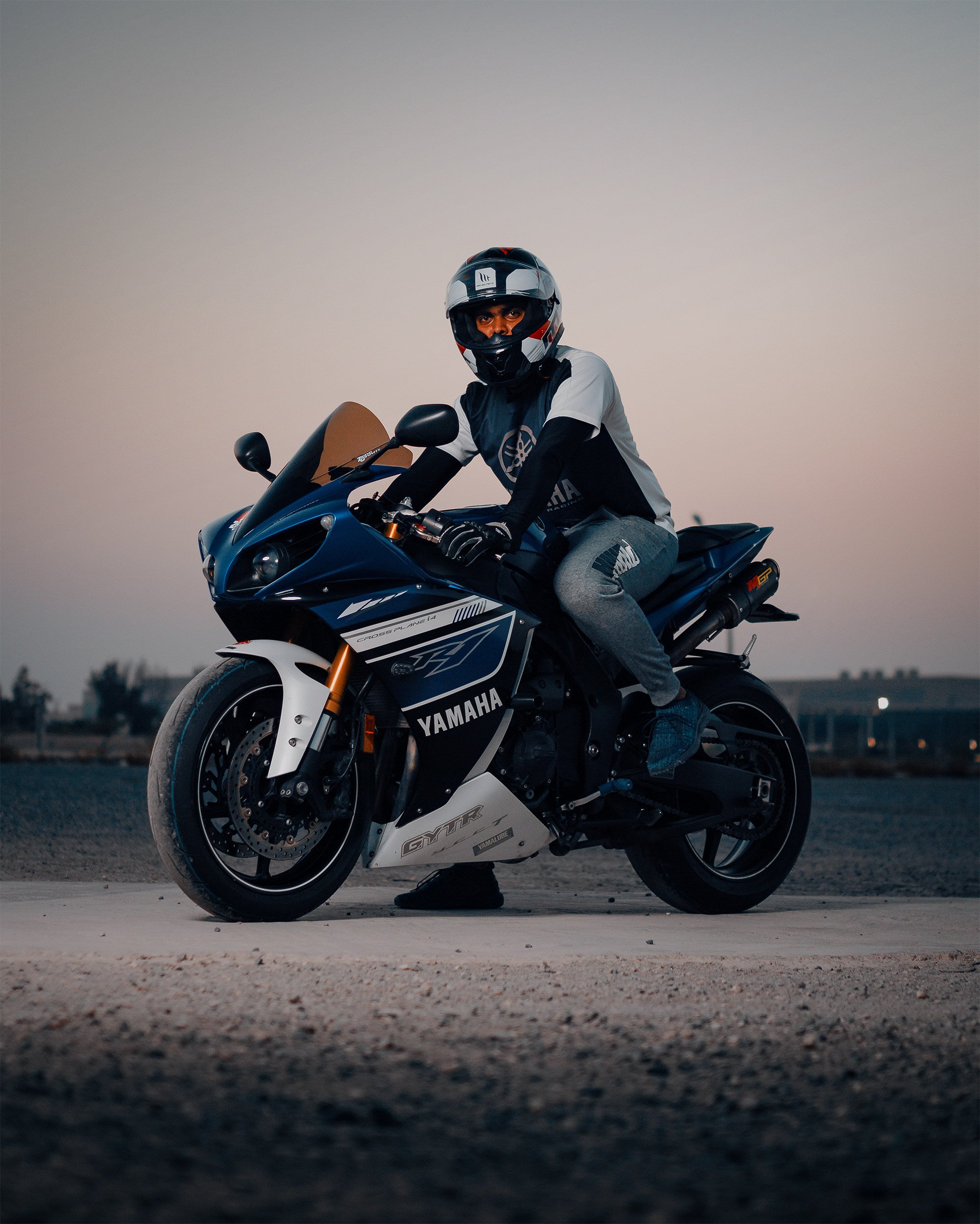 Person wearing a helmet and casual clothes sitting on a Yamaha motorcycle outdoors at dusk.