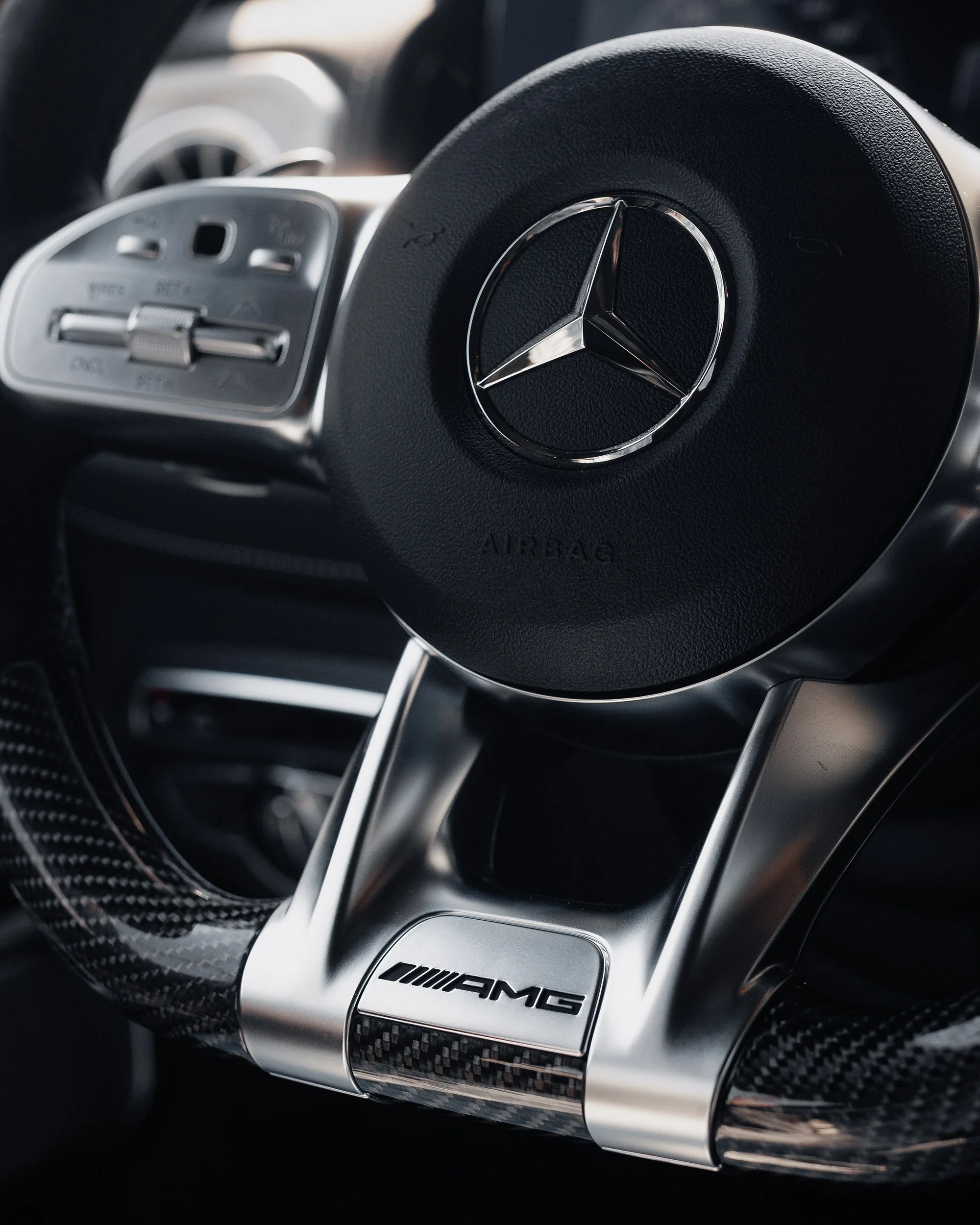 Close-up of a Mercedes-Benz steering wheel with AMG branding and carbon fiber accents.
