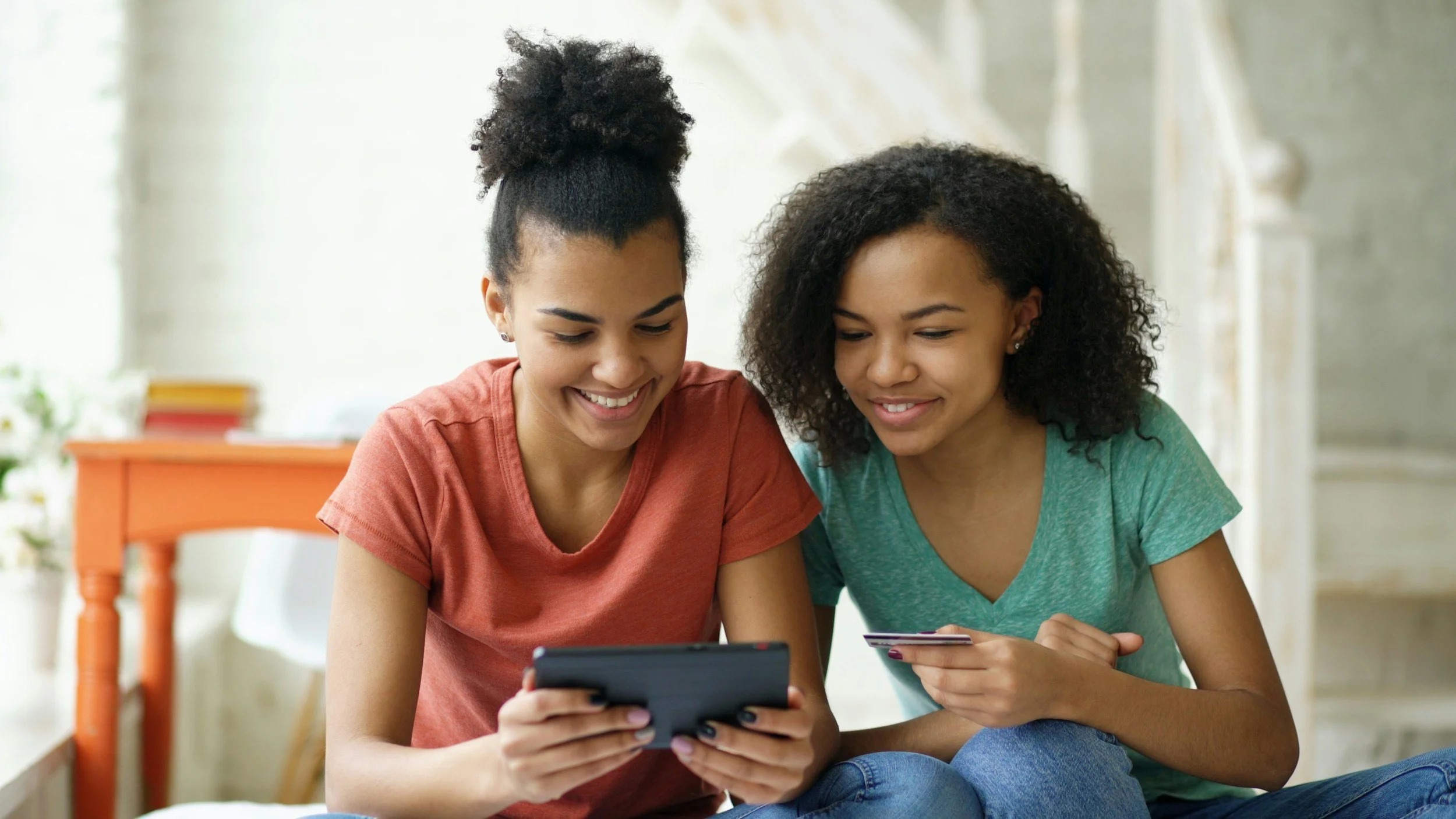 Two women sitting closely together, smiling and looking at a smartphone and a credit card.