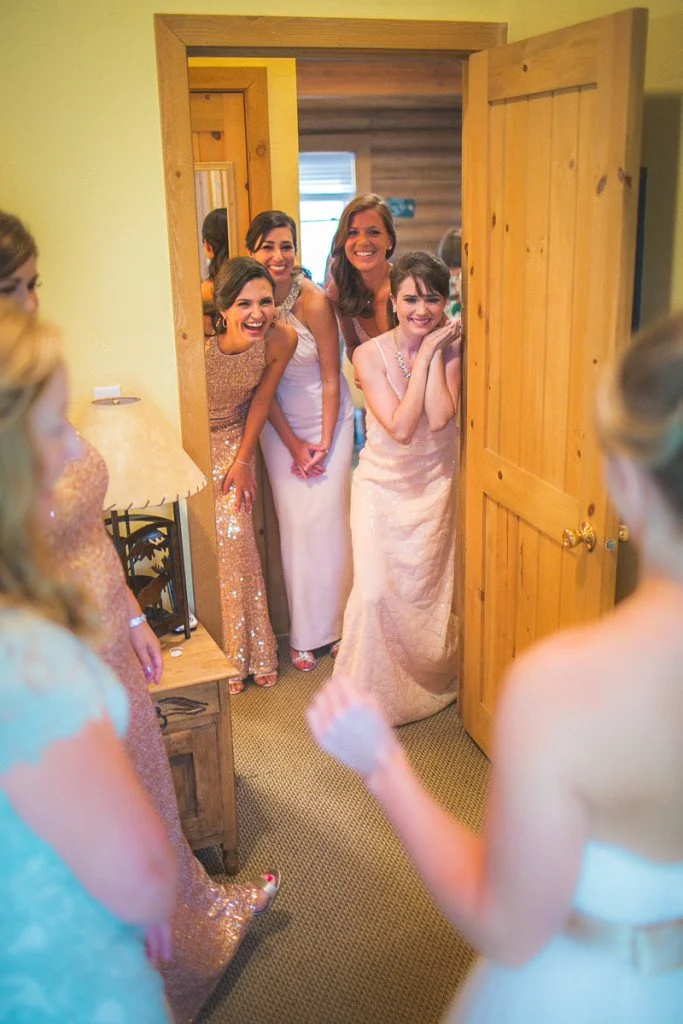 A group of women in elegant dresses standing in a doorway, smiling and celebrating together.