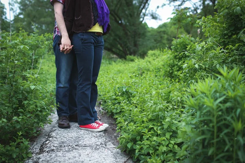 People standing on a stone path surrounded by green bushes in a natural outdoor setting.