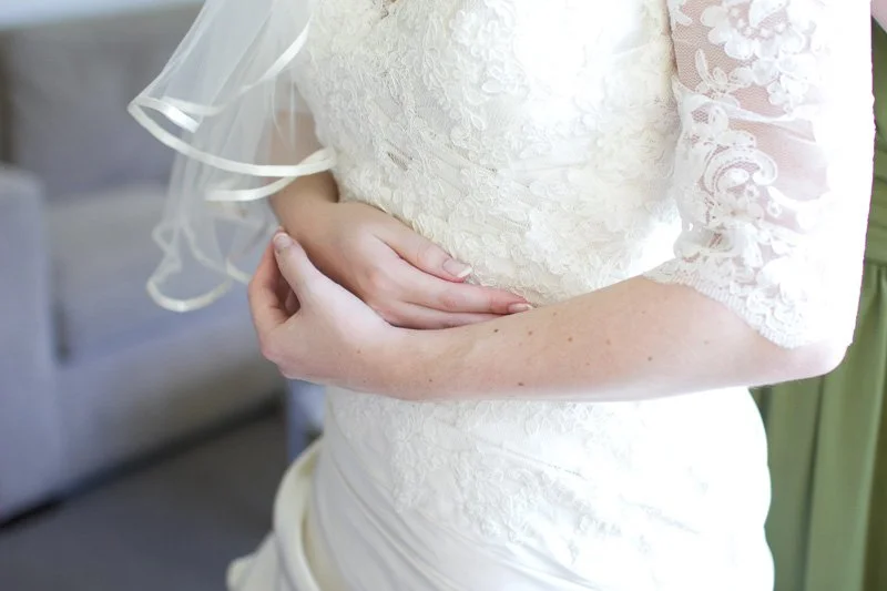 A person in a white lace dress, with their hands resting on their stomach, possibly indicating pregnancy.