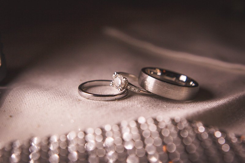Close-up of two wedding rings and a diamond engagement ring on a satin fabric, with a blurred background of jewelry.