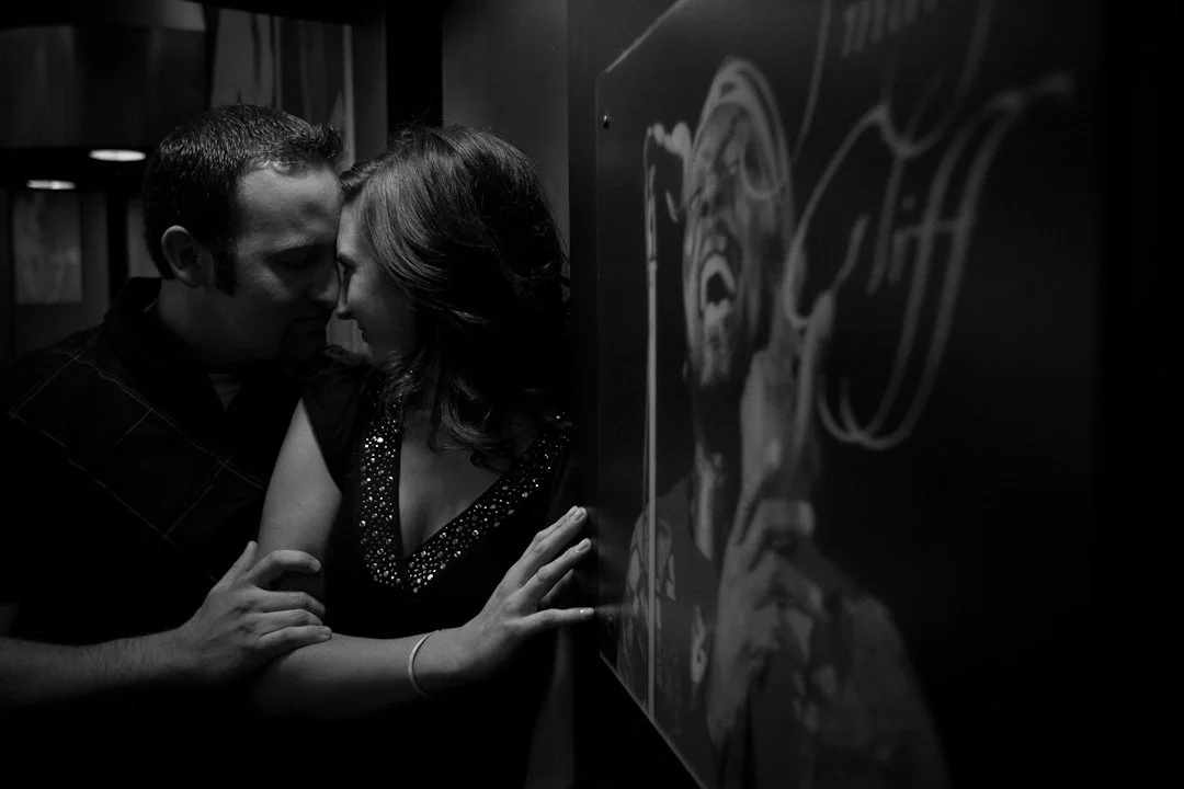 A man and woman with close eyes, touching foreheads together in an intimate moment, standing near a wall with a chalk drawing of a face.