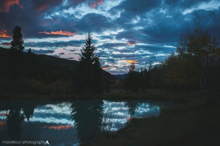 Sunset over a lake with reflections of trees and a partly cloudy sky.