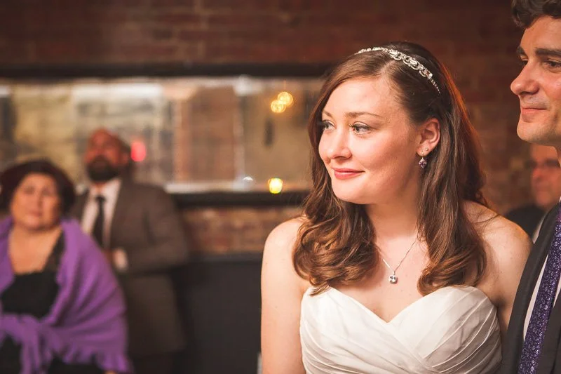 Bride and groom standing together at a wedding reception with guests in the background.