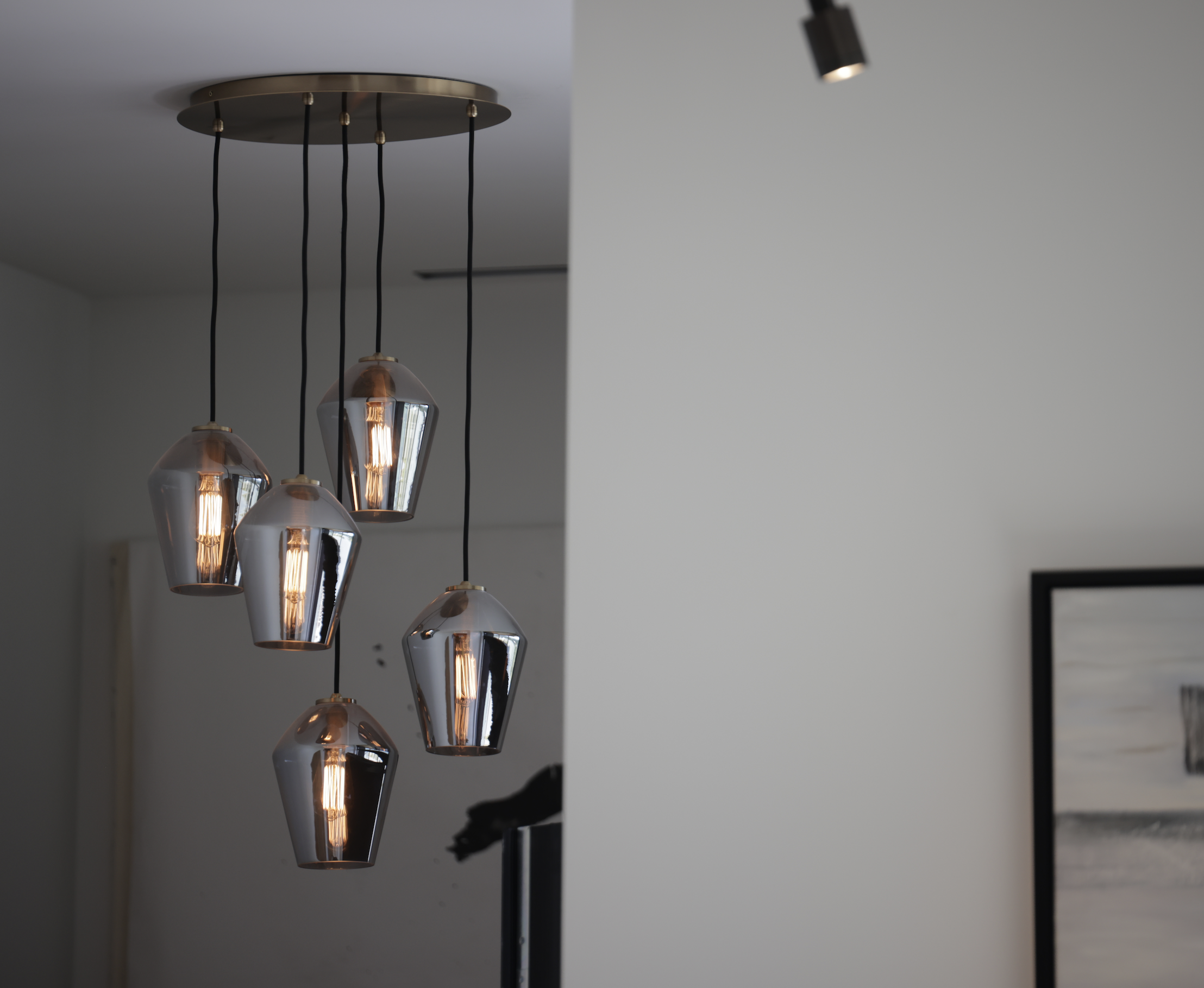 Modern pendant light fixture with six metallic lampshades hanging from black cords.