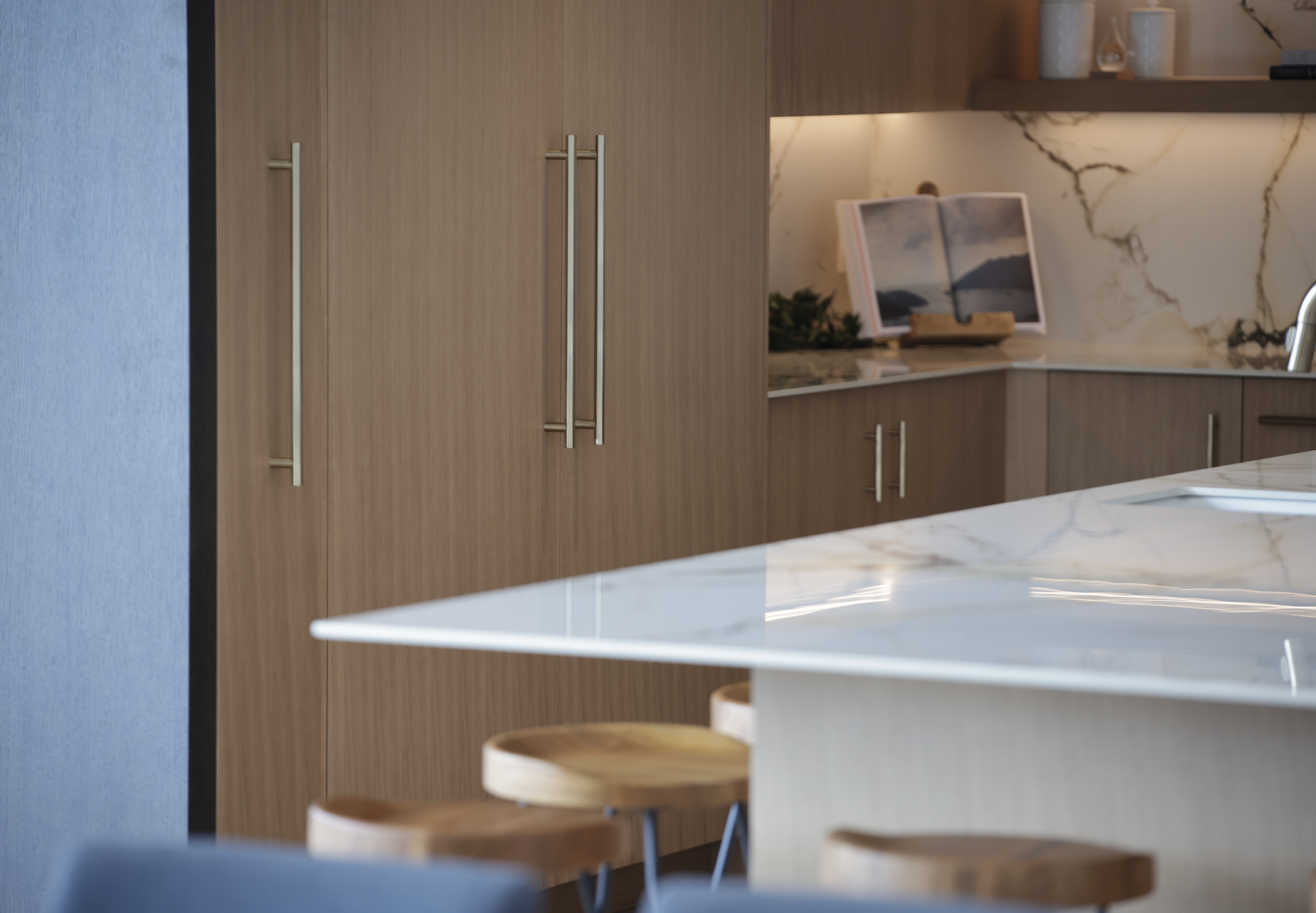 Modern kitchen with wooden cabinets, marble countertops, and barstools.