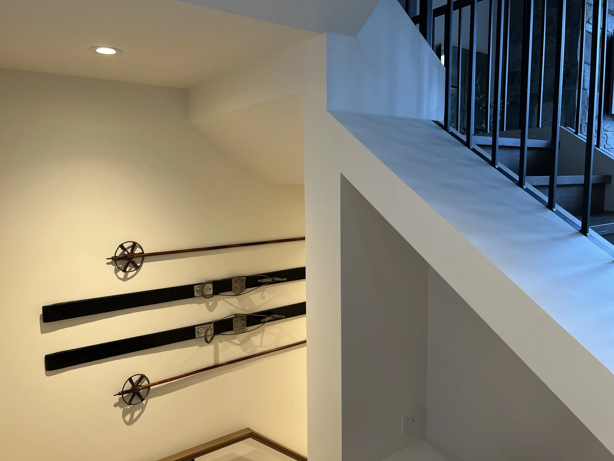 Decorative wall with three medieval style swords mounted above a wooden frame, next to a staircase with black metal railing, in a modern interior.