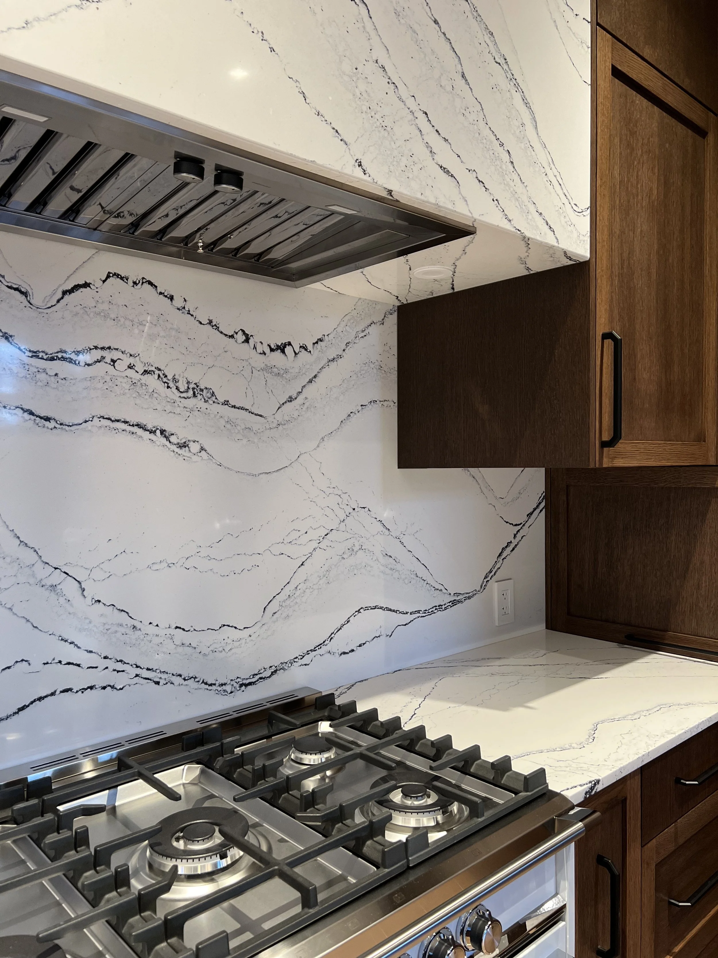 Kitchen with a marble-style backsplash and countertop, gas stove, and wooden cabinets.