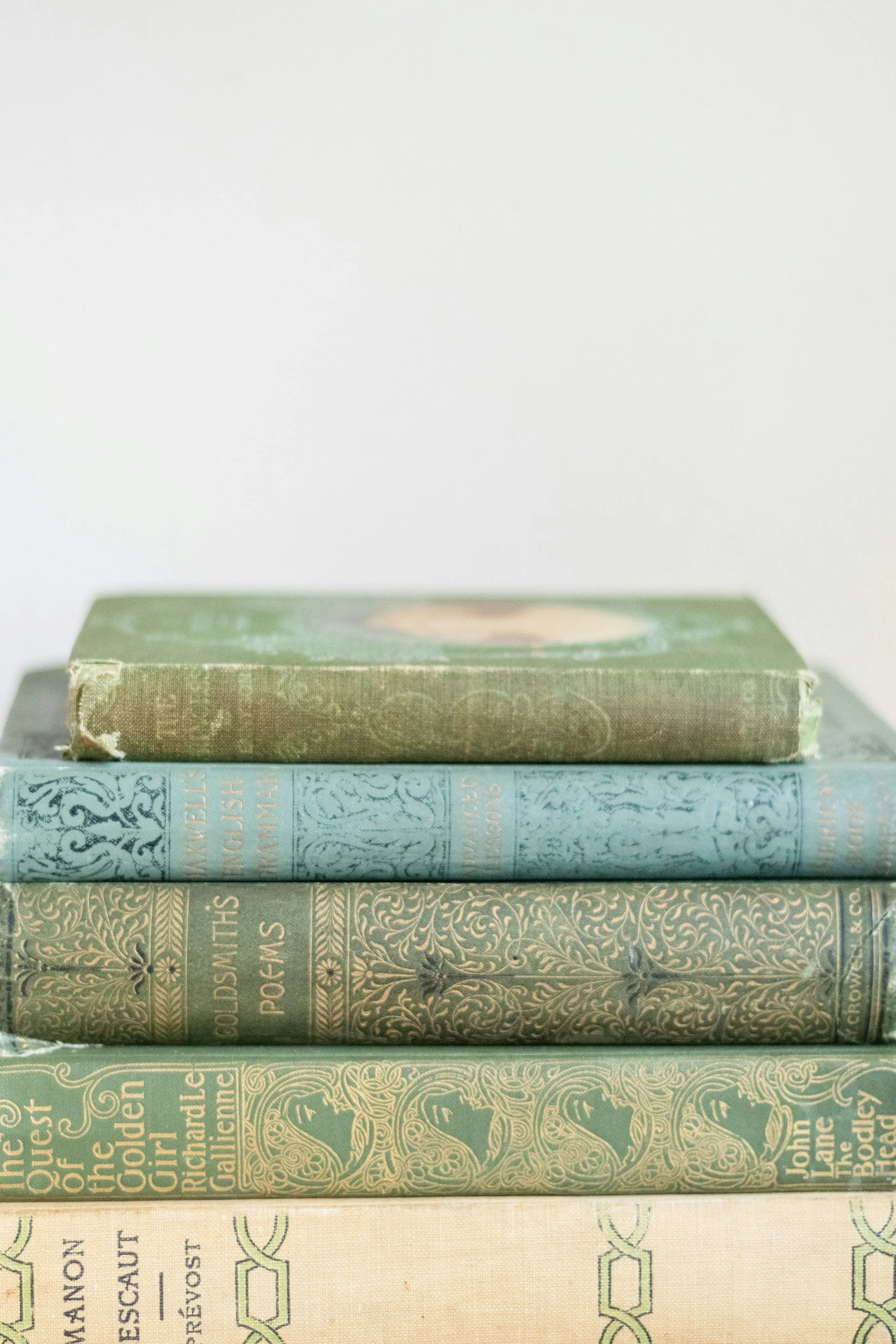 Stack of four vintage hardcover books with worn cloth covers in green, blue, dark green, and beige colors, placed on a white surface.