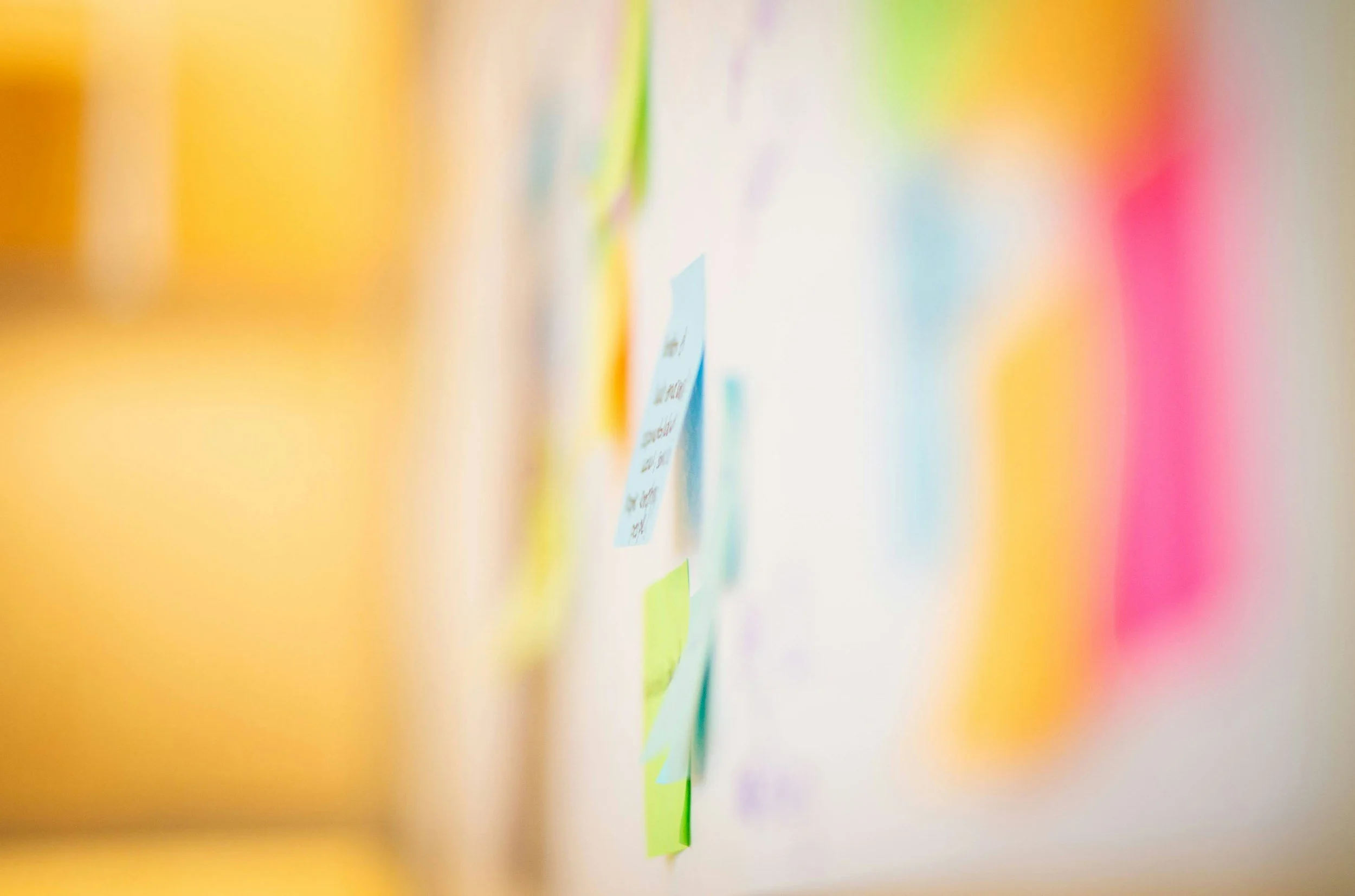 Blurred image showing a wall covered with colorful sticky notes and papers.