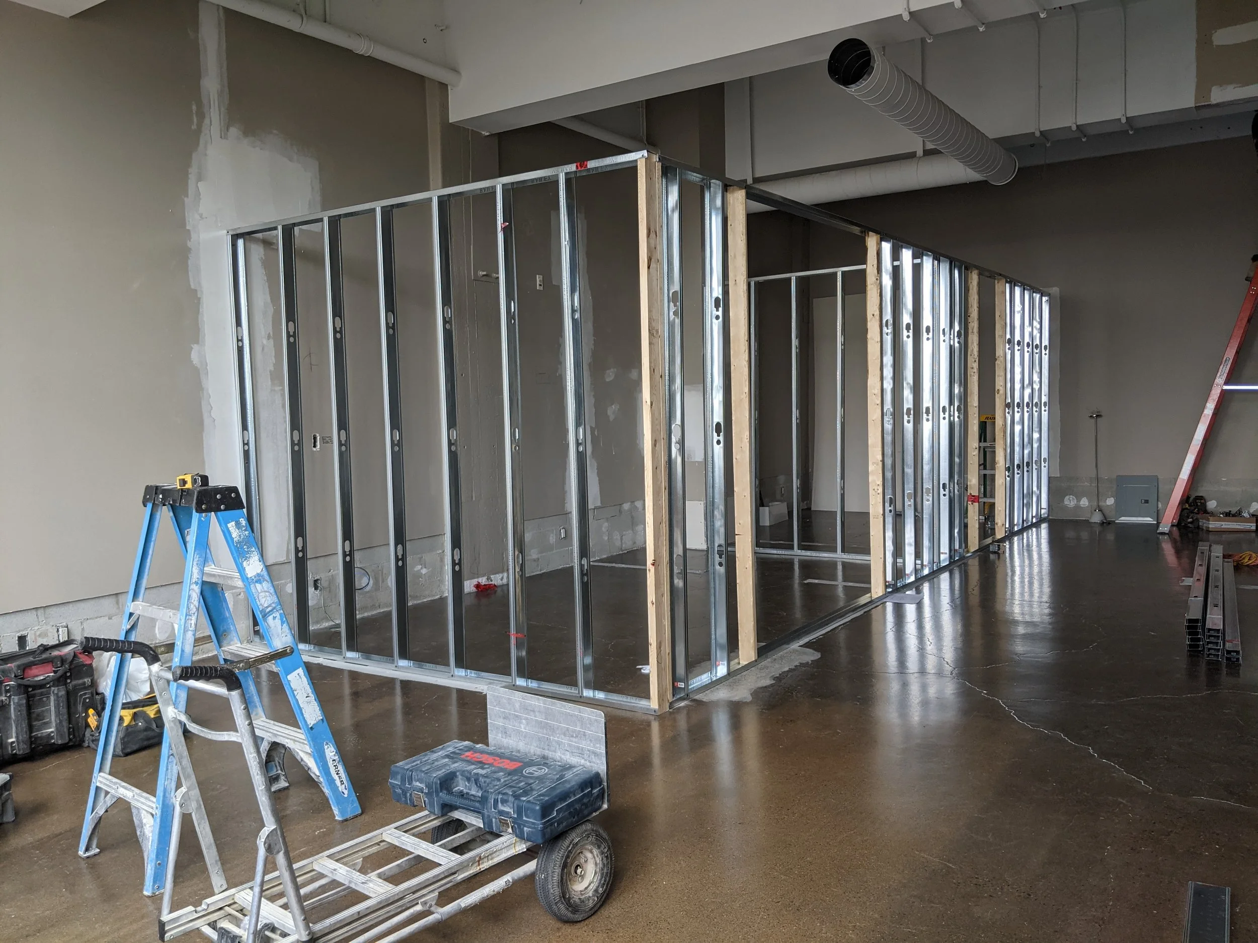 Interior of a building under construction with metal framing for walls, a stepladder, and construction tools on the floor.