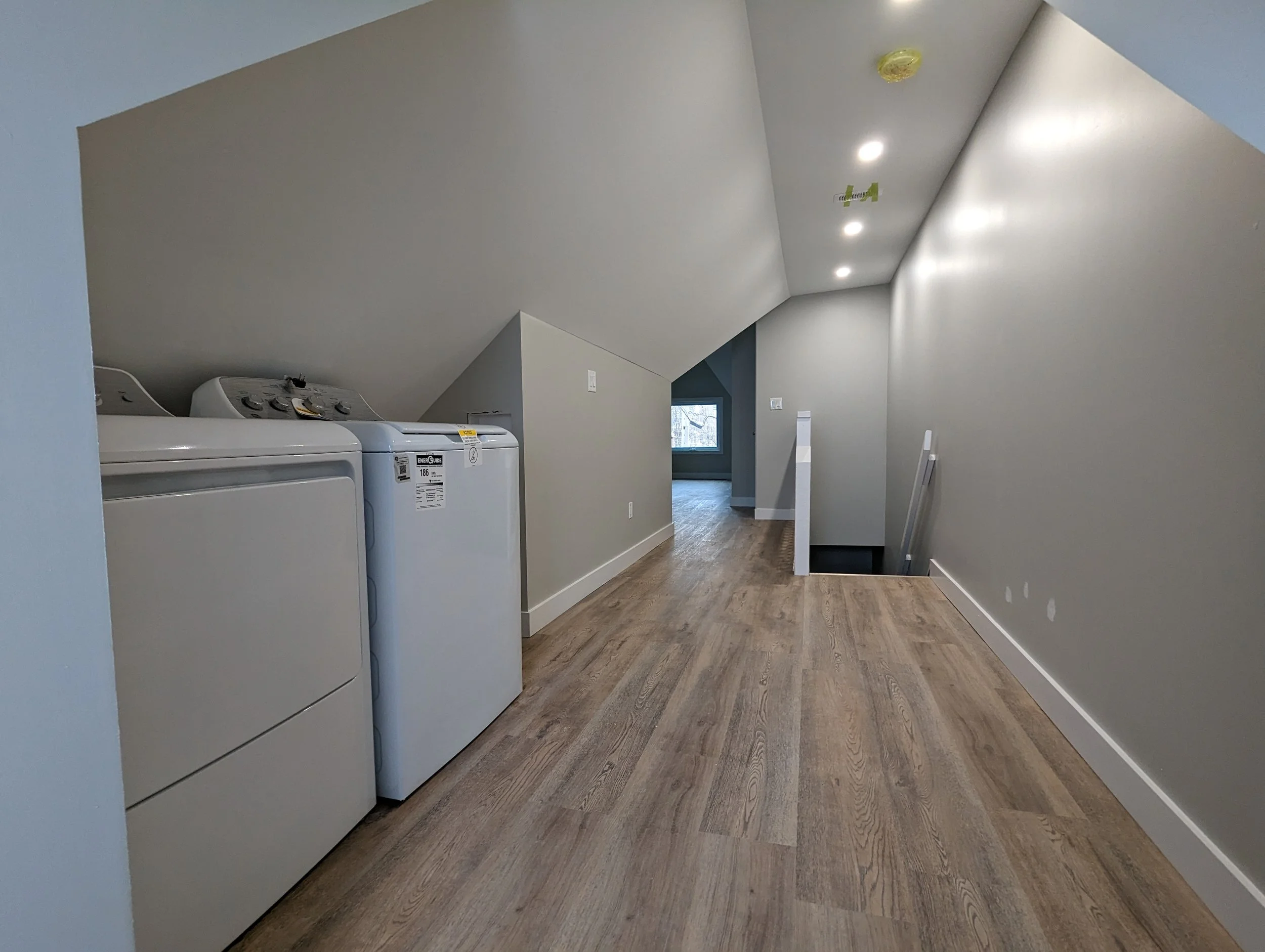 Laundry room with washer, dryer, and wood flooring, sloped ceiling, and recessed lighting.