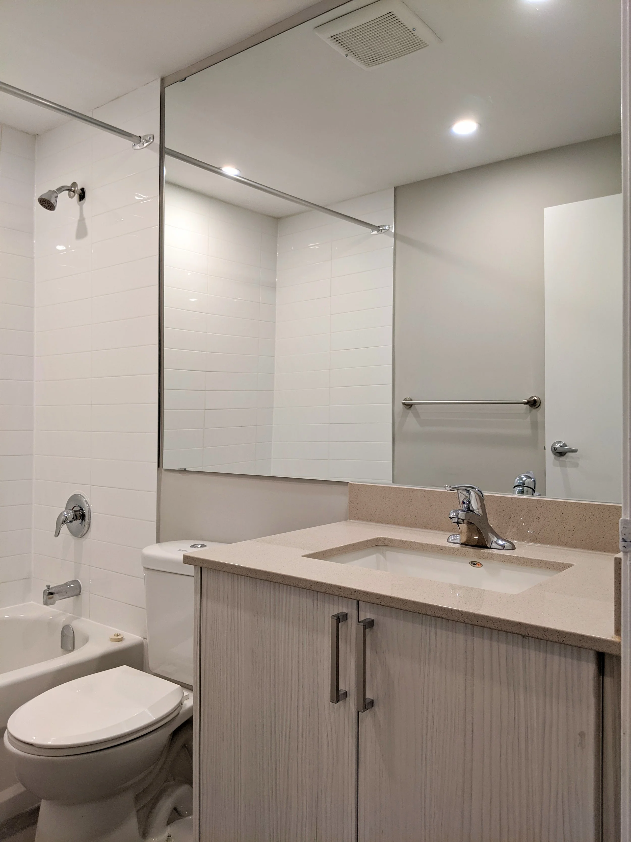 A bathroom with a mirror, sink, toilet, and bathtub with showerhead.