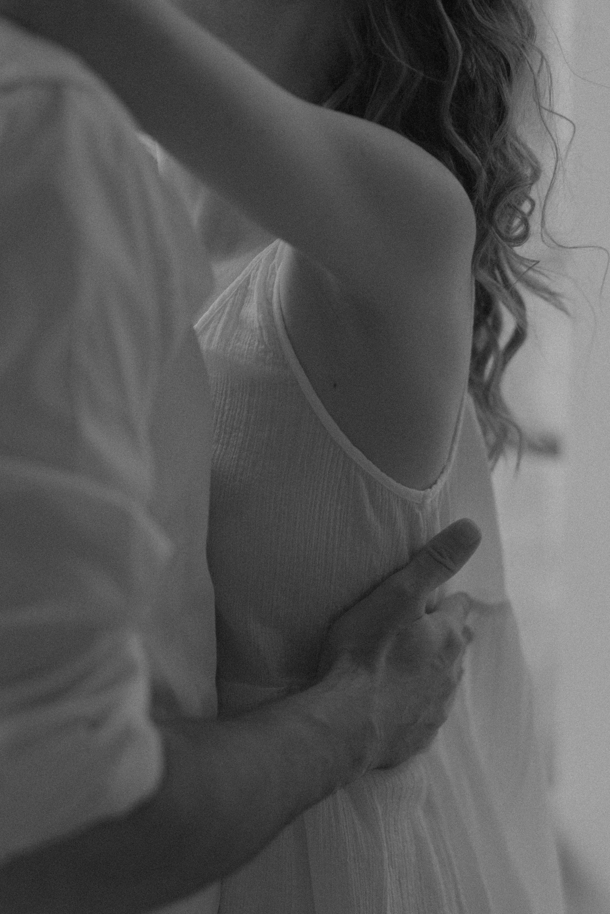 A person with curly hair wearing a sleeveless top, resting their arm on their head, in a grayscale photo.