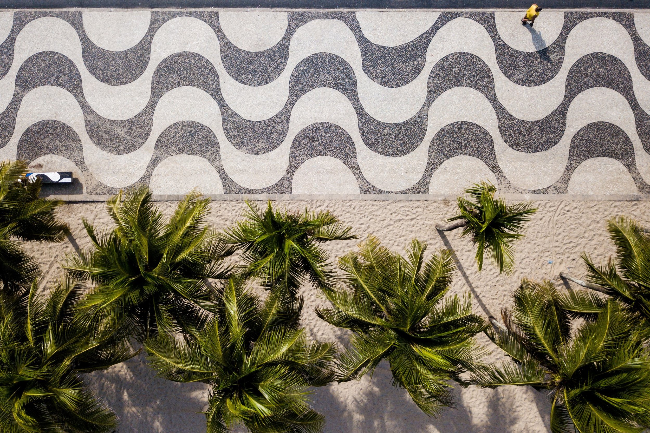 An aerial view of a beach walkway with a patterned black and white design, bordered by lush green palm trees.