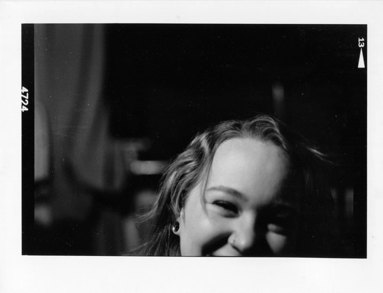 Black and white photo of a young woman smiling, showing only part of her face with a focus on her eyes, eyebrows, and wavy hair.