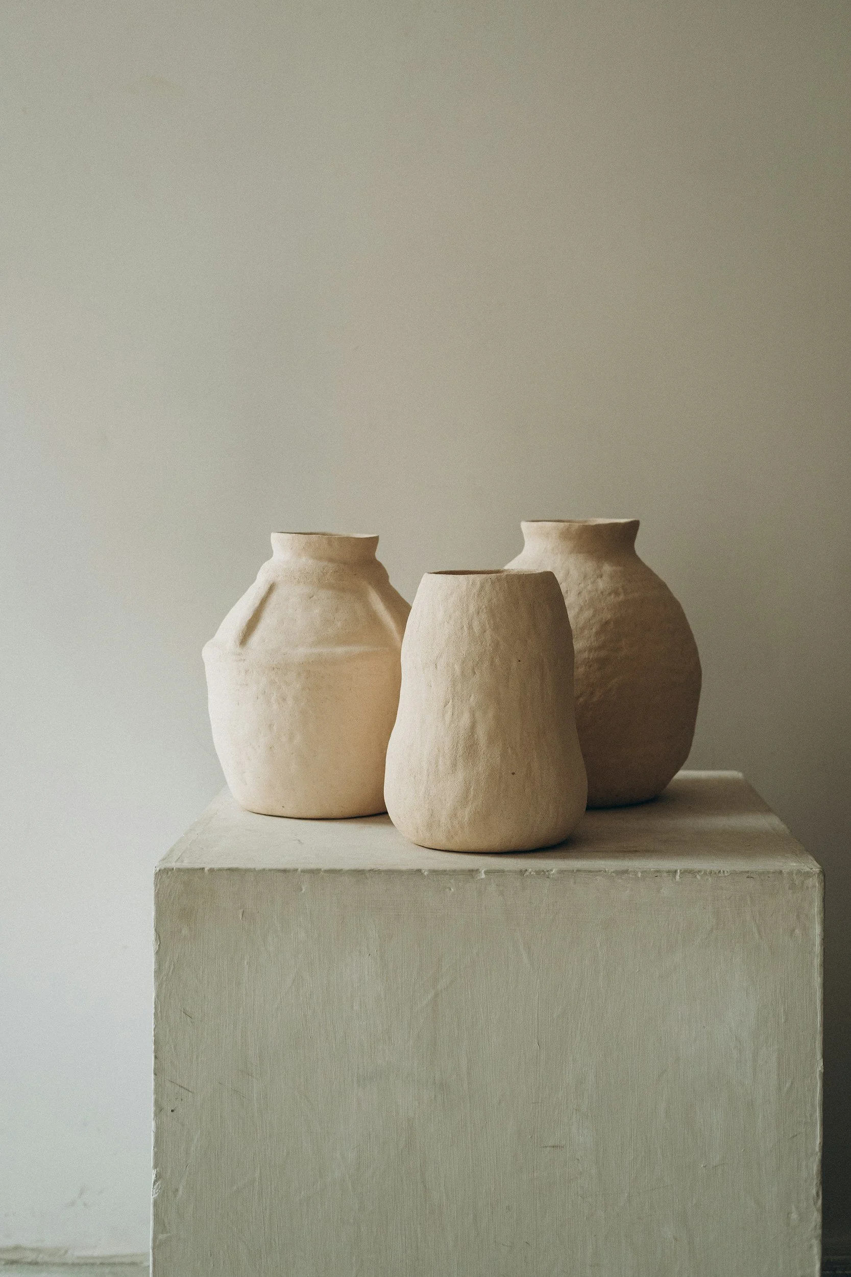 Three beige ceramic vases on a white pedestal against a plain background.